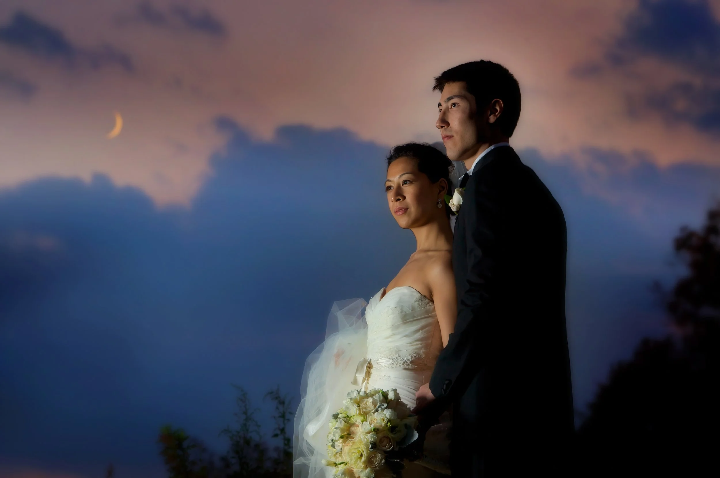 Bride and groom pose on a hillside at Glen Island Harbour Club beneath a crescent moon