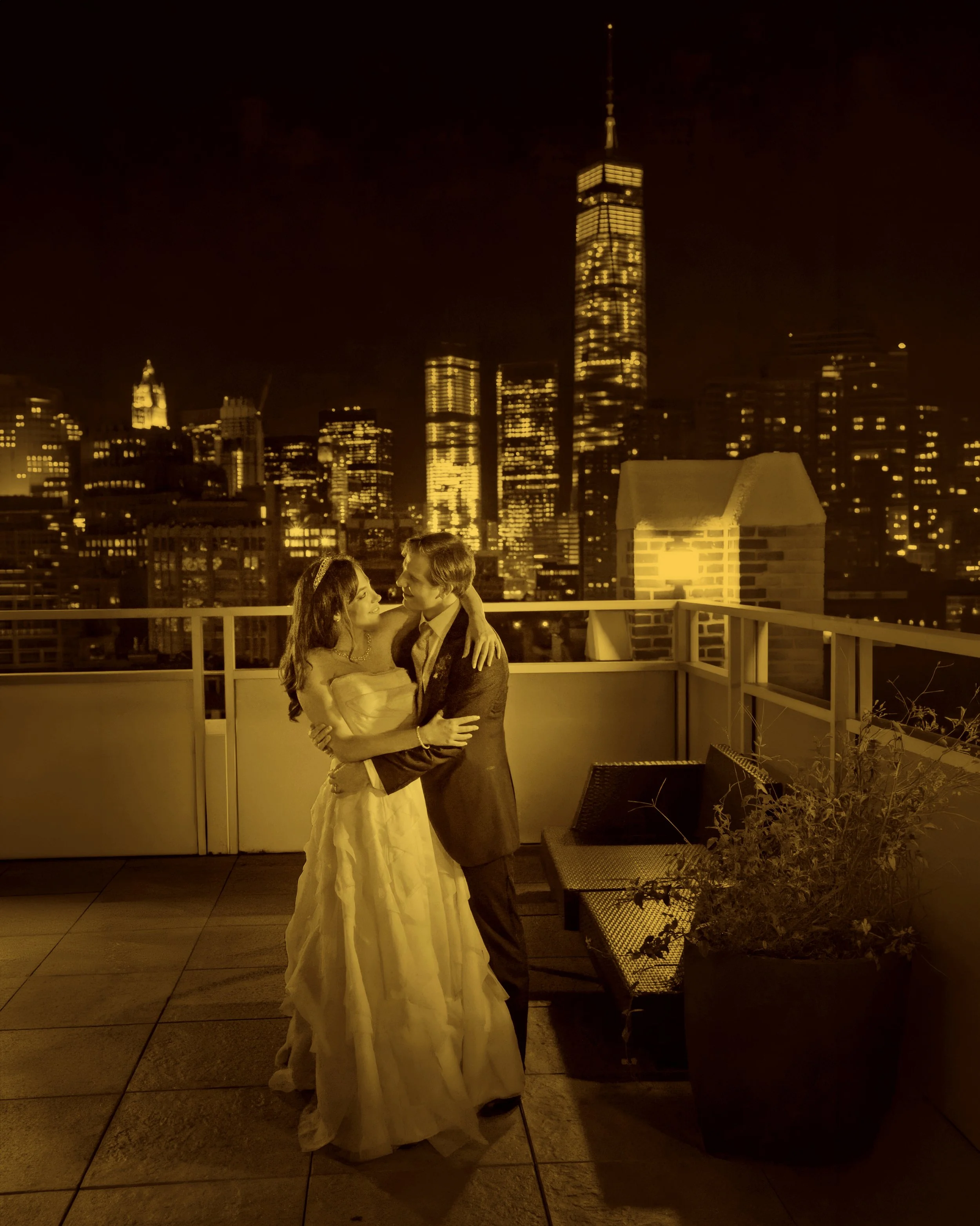 Bride and groom embracing on the rooftop with the illuminated Manhattan skyline in the background in a fine art wedding photograph.