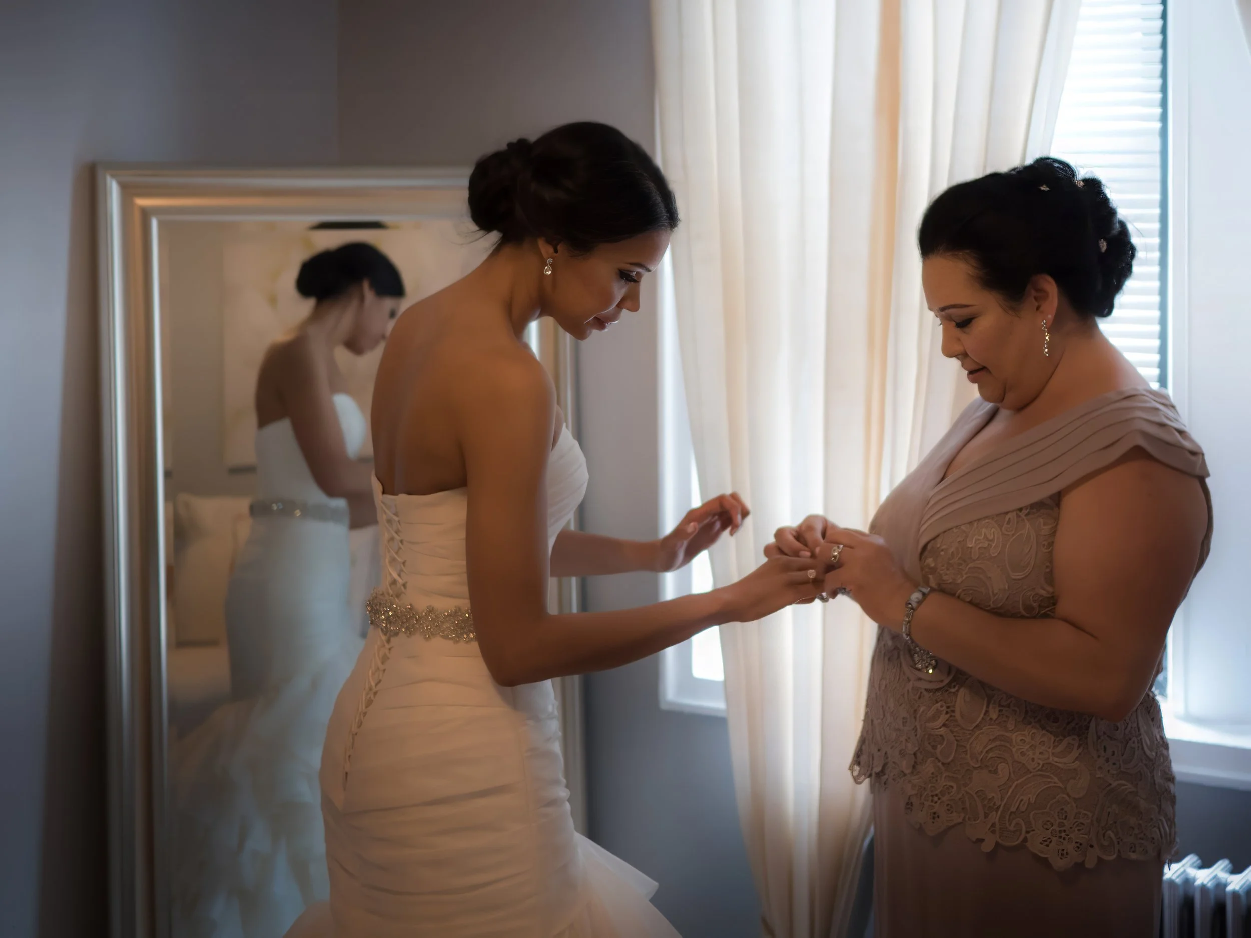 Mother of the bride assists her daughter with wedding jewelry during getting ready at their family home in New York City.