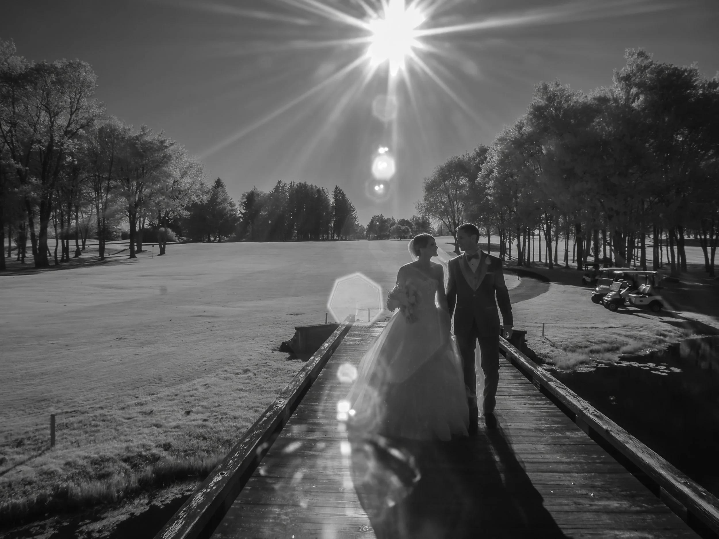 Bride and groom walk in silhouette with sun flaring in the background at Salem Golf Club.