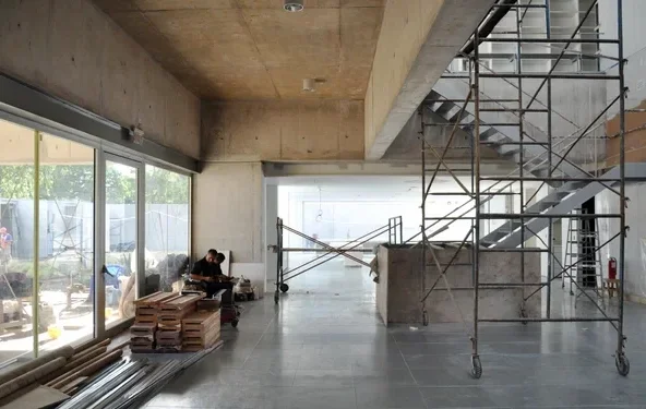Interior of a building under construction with scaffolding, concrete structure and large glazing, showing on‑site supervision and ongoing architectural work