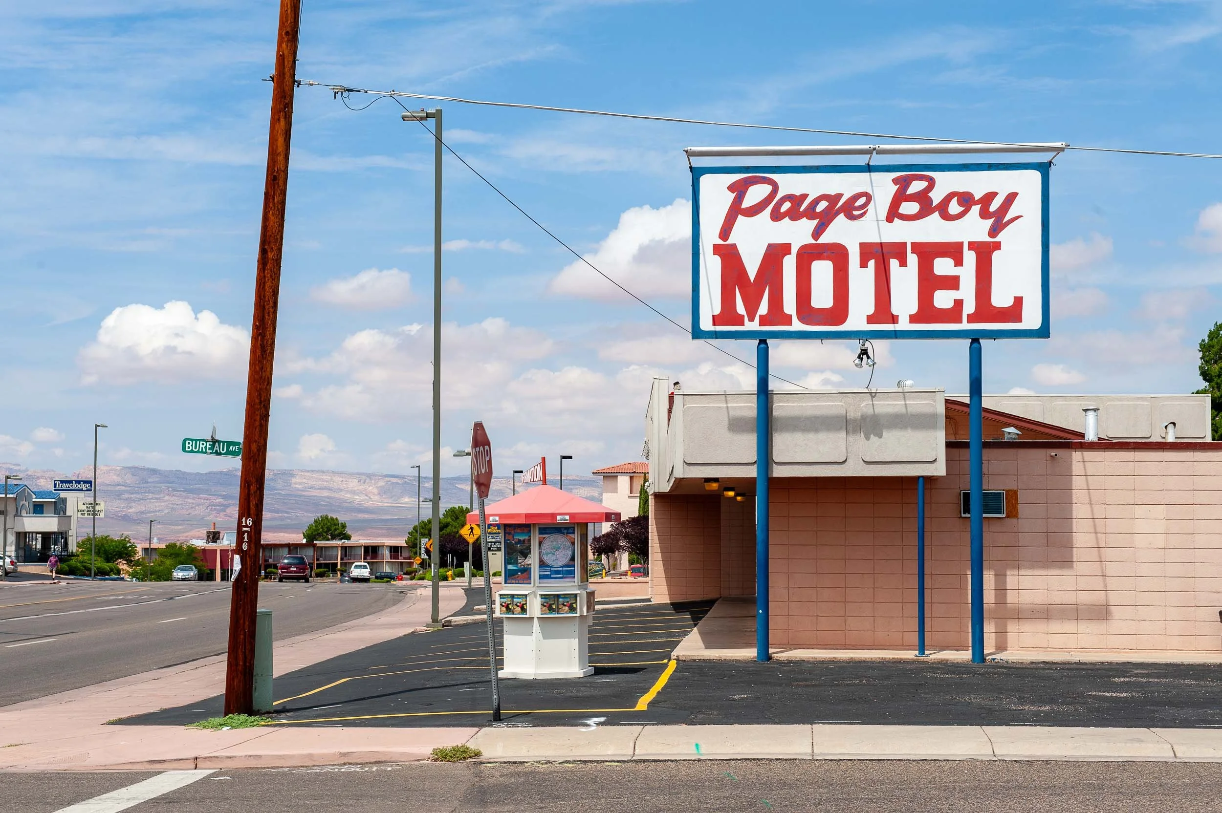 Street view showing a large sign for Page Boy Motel, a telephone booth or info display, and part of a beige building with red roof in the background.