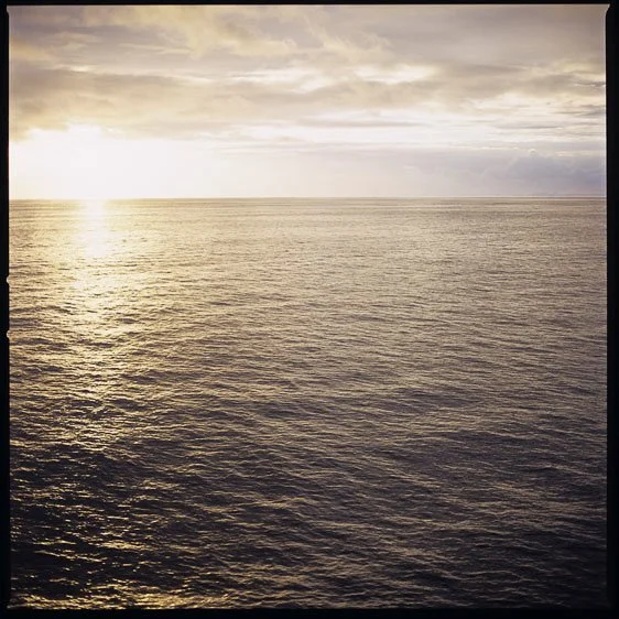 Calm ocean water with sunlight reflecting on the surface and cloudy sky above.