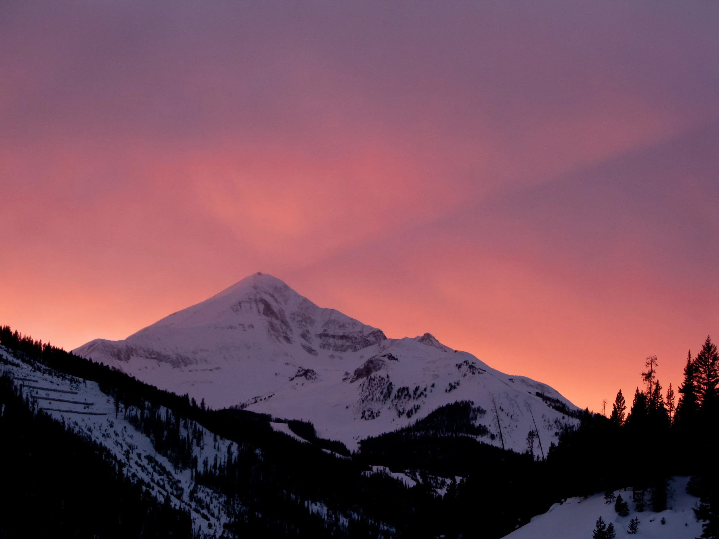Snow-covered mountain at sunset with a pink and purple sky.