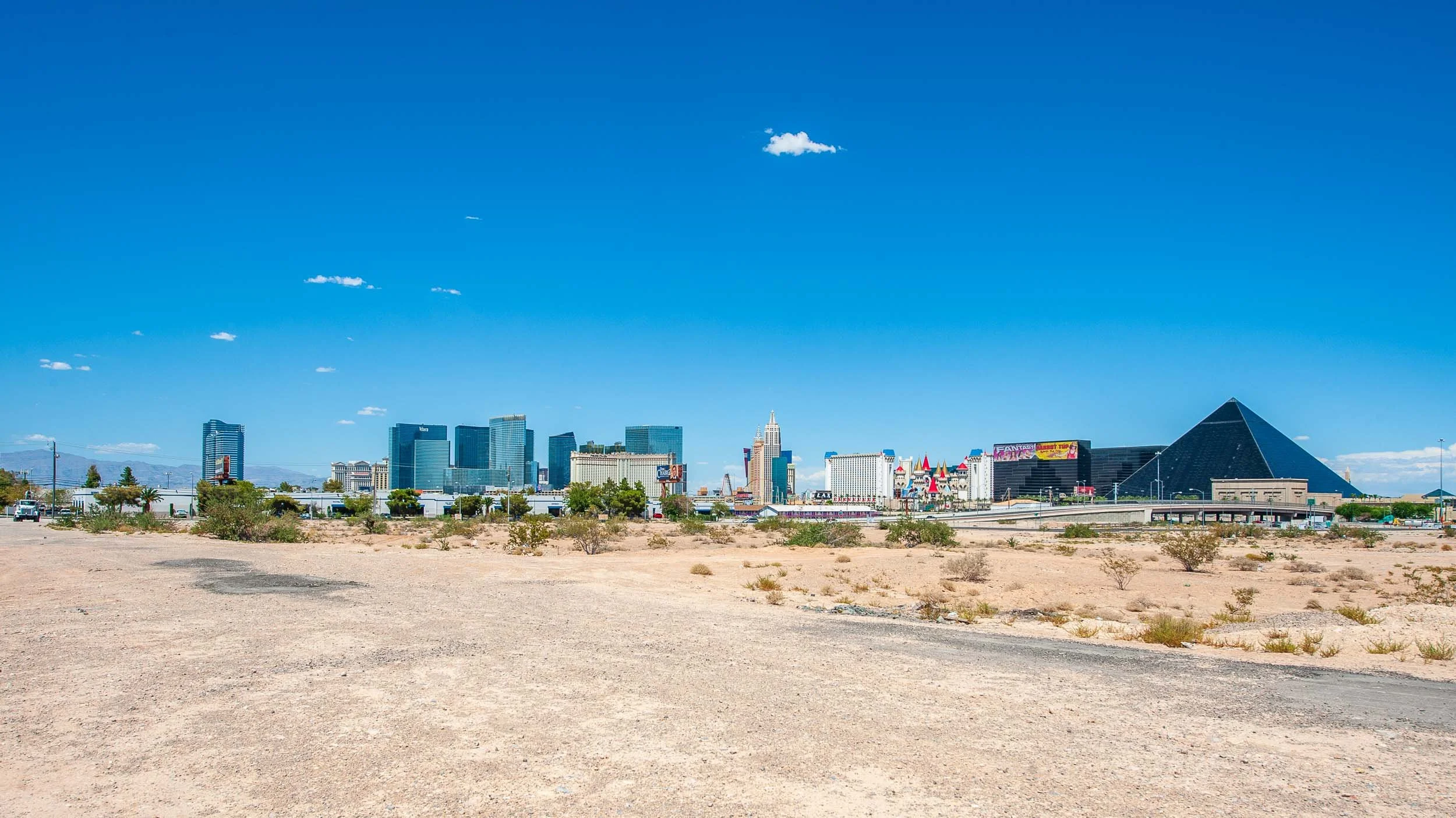 Las Vegas skyline with hotels and casinos, viewed from a desert foreground under a clear blue sky.