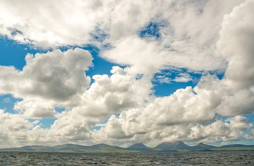 A cloudy sky over a body of water with mountains in the distance.