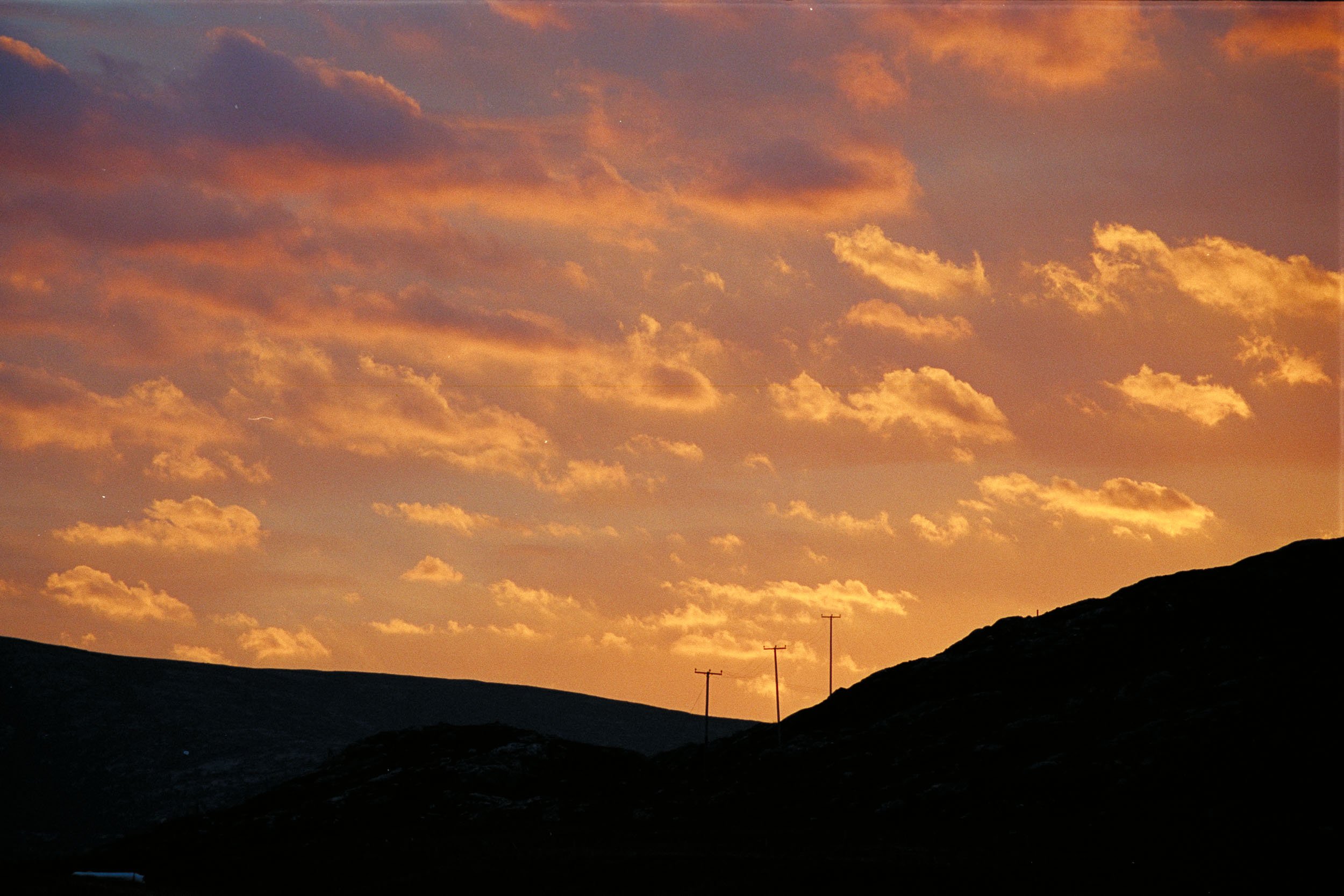 Sunset sky with orange clouds, silhouetted hills, and three utility poles.