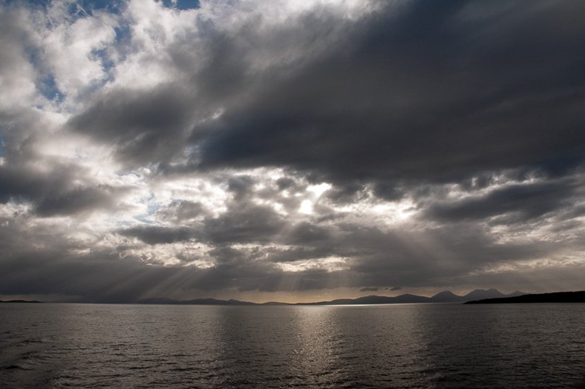Overcast sky with dark clouds over a body of water, with mountain silhouettes in the distance.