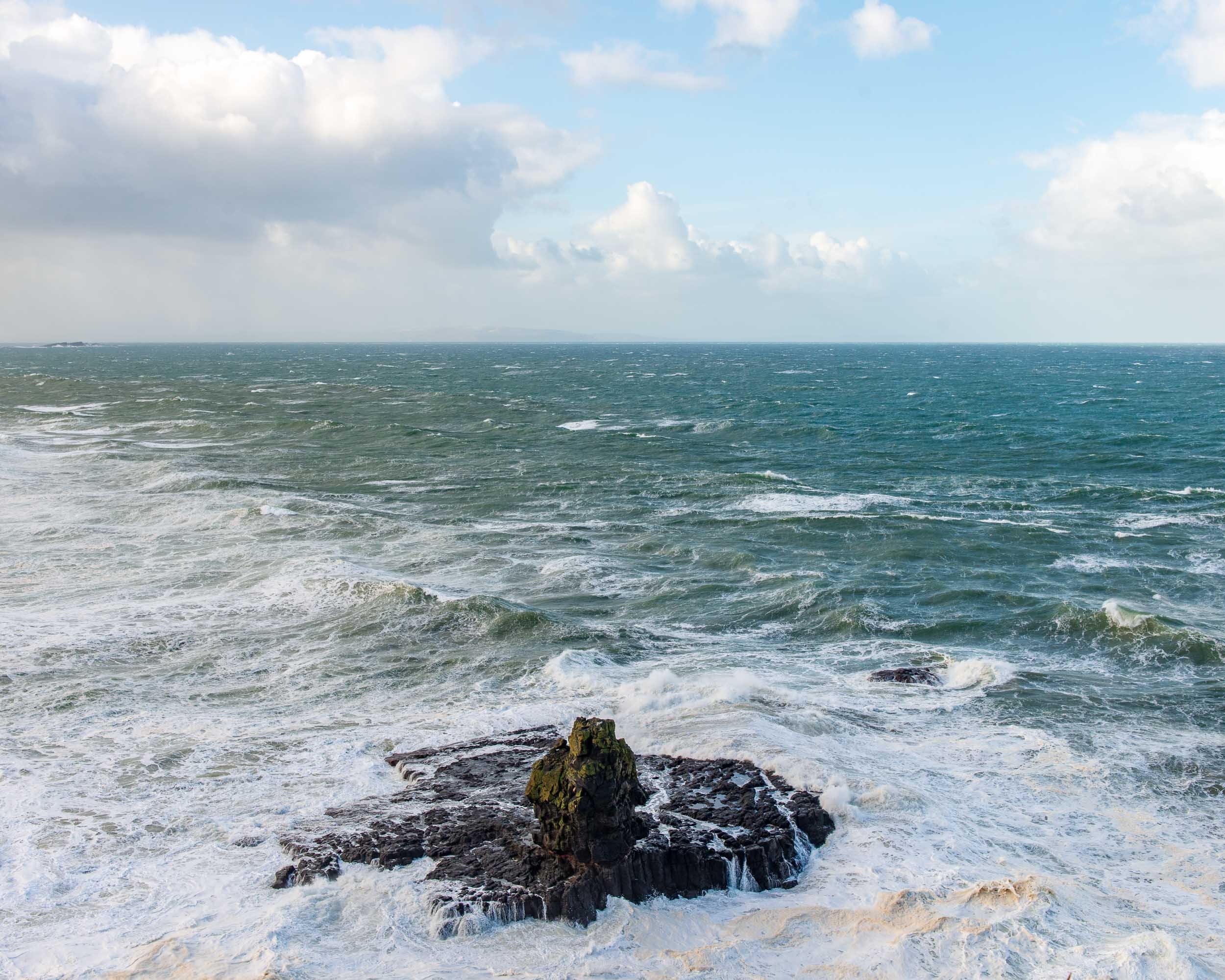 Ocean waves crashing against rocks under a partly cloudy sky.