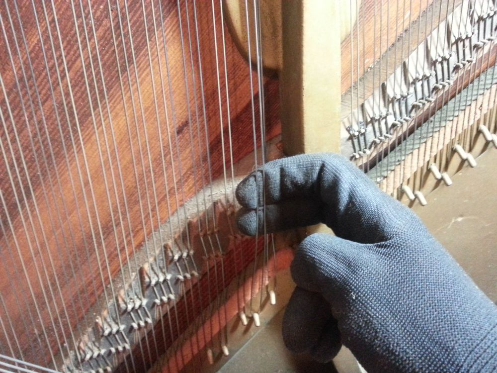 Holding tension on the strings while turning the tuning pins. I wear gloves to prevent any moisture on my hands from causing the strings to rust.