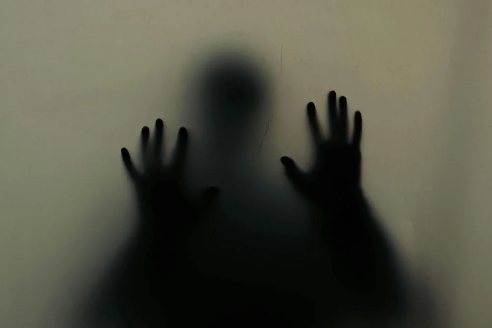 Image of person pressing hands against glass as if to escape.