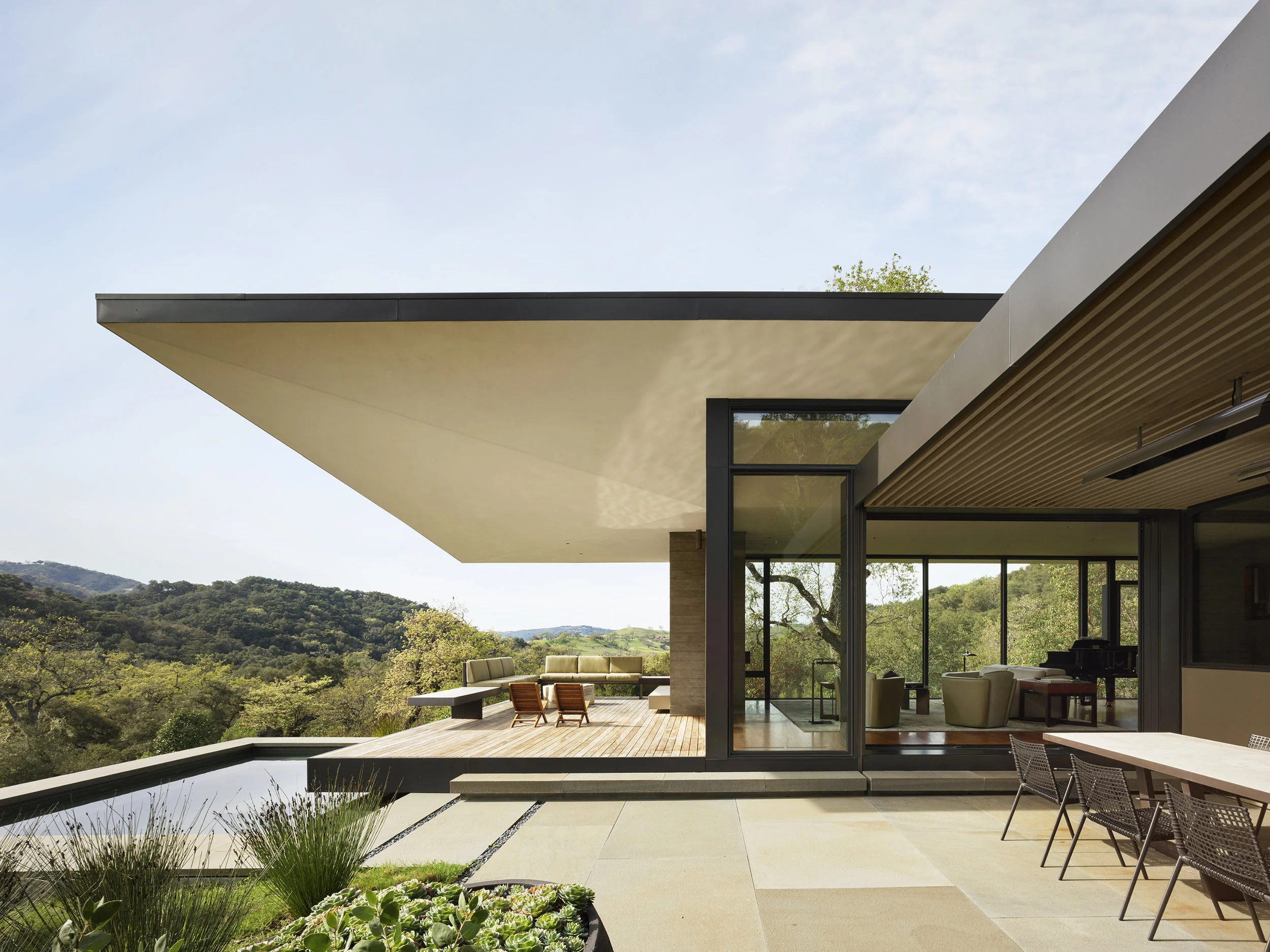 Nestled between groves of oak and madrone trees on a steeply sloping site in a nature preserve, the eastern corner of the house burrows into the hillside while the west cantilevers dramatically over the falling topography below. The unique shape of the roof is derived from both context and performance: from the exterior, the roof appears as a simple shed roof inspired by the local agrarian vernacular while the interior is sculpted in response to both natural sunlight and the quality and scale of the interior spaces. Completed by Aidlin Darling Design; Adrienne Swiatocha, Project Architect