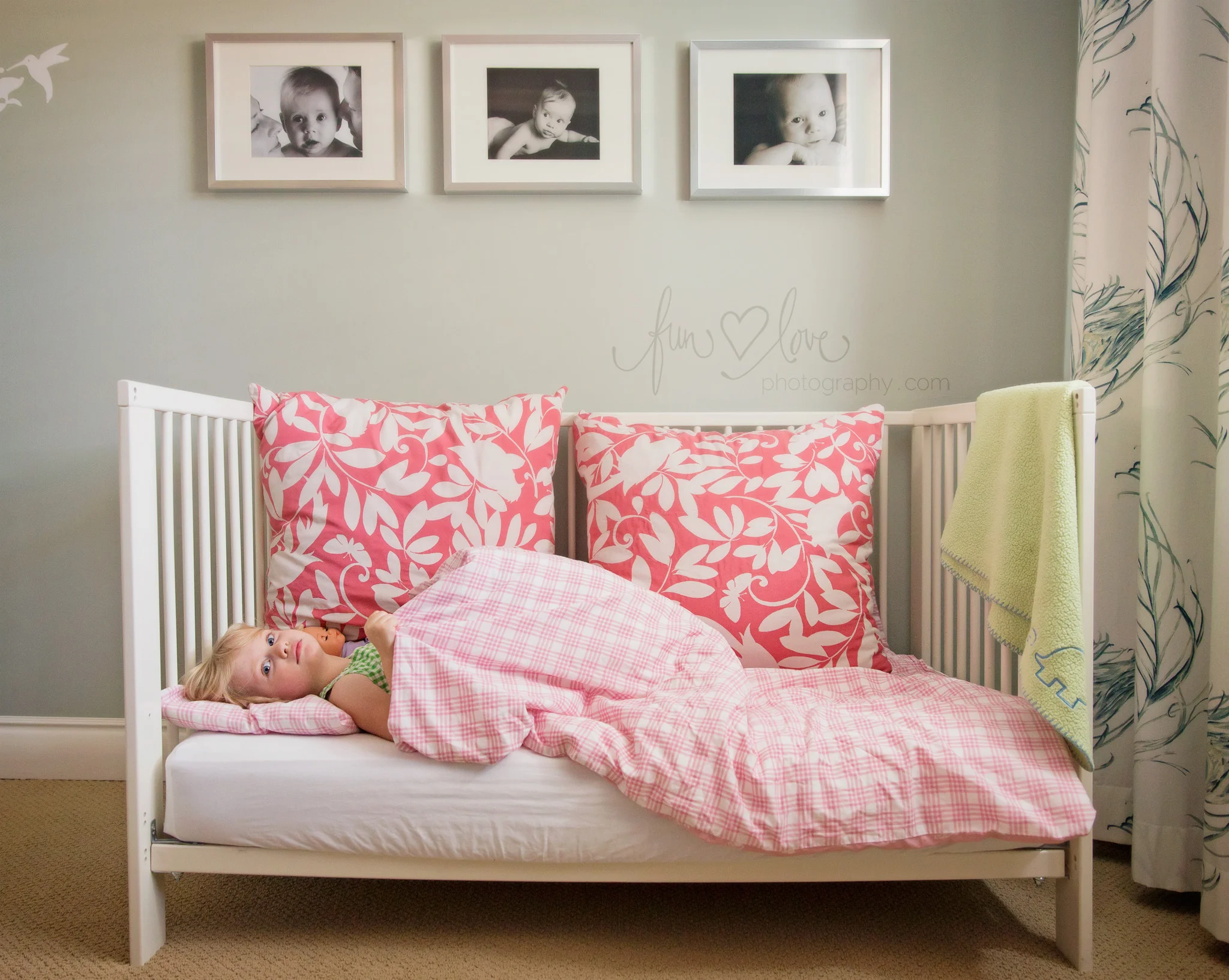 Girl in crib bed with her baby pictures on the wall
