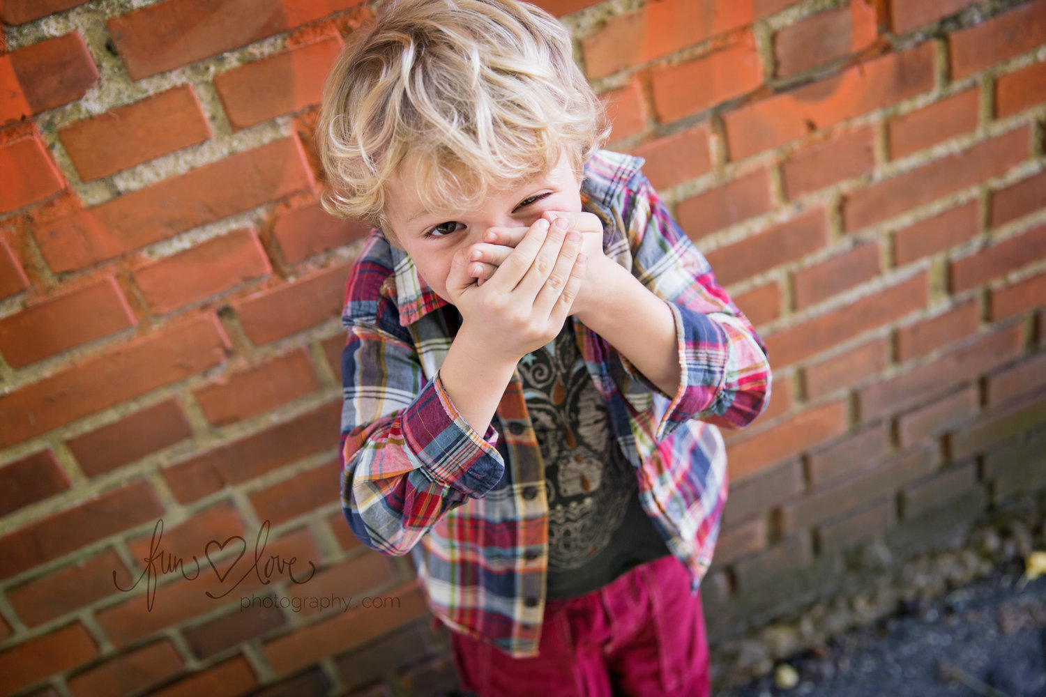 boy in plaid shirt against brick wall laughing covering mouth