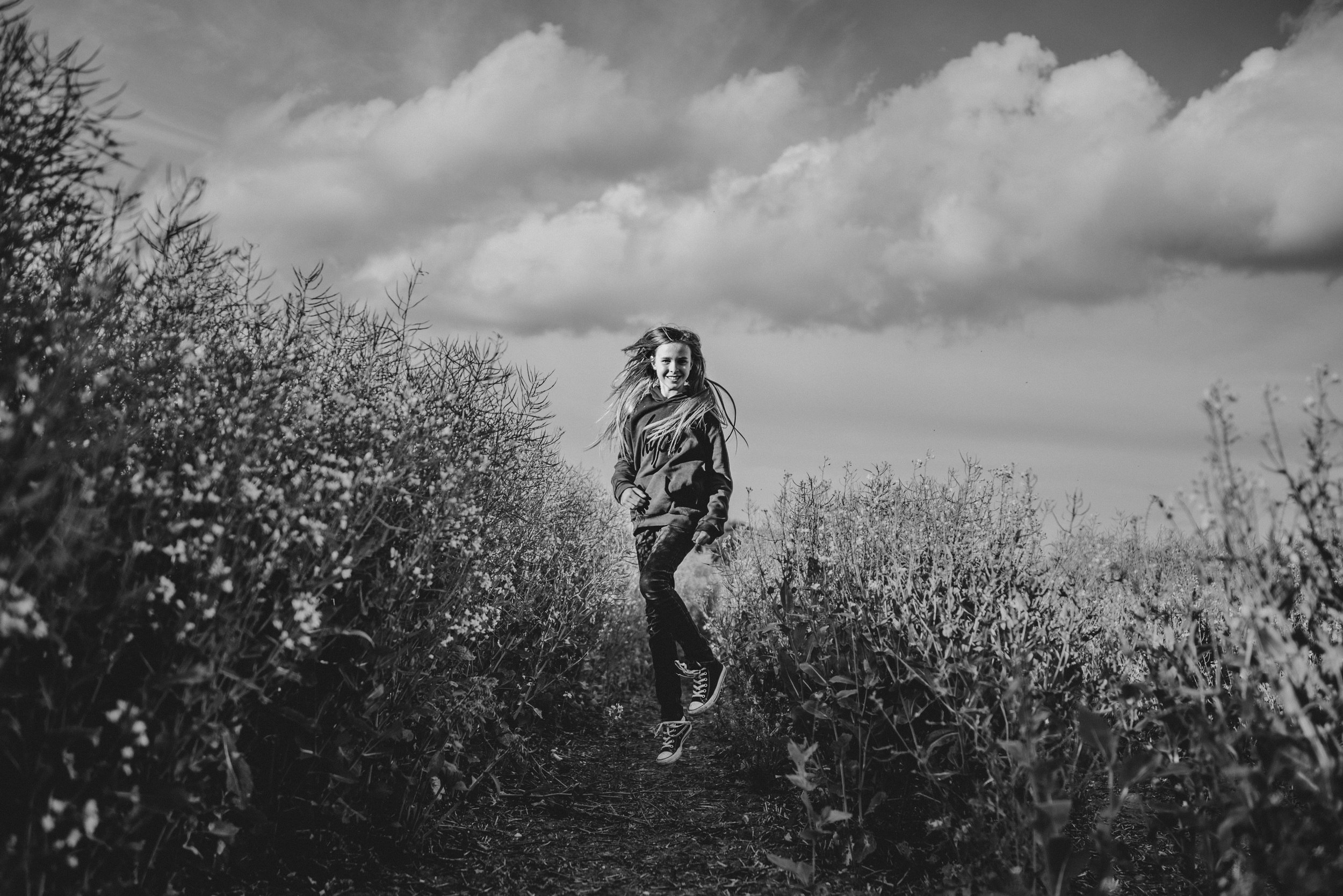 Tween girl jumps in field cloudy sky Essex UK Documentary Portrait and Lifestyle Photographer