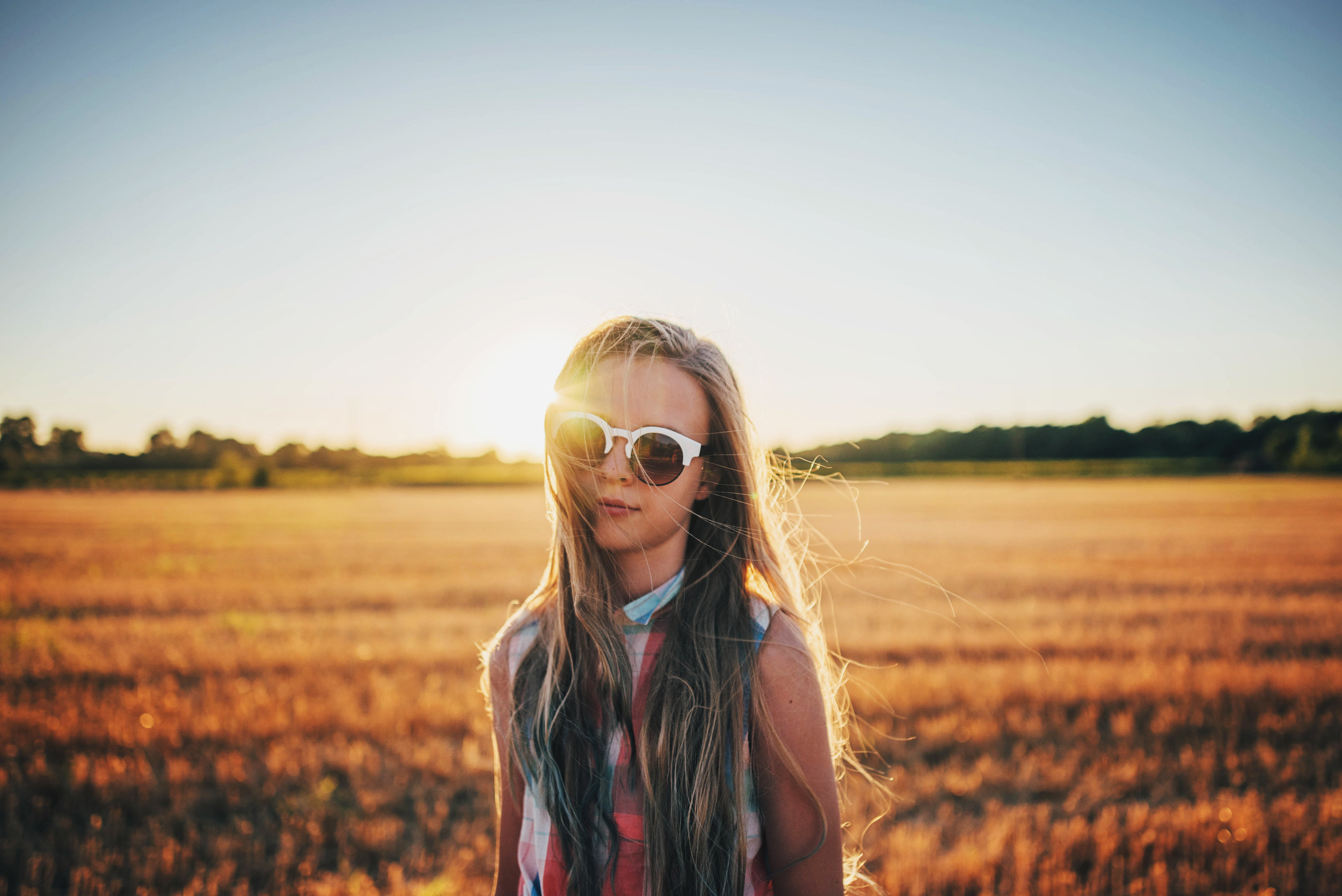 Young girl in Sunglasses stands in field at sunset Essex UK Documentary Portrait Photographer