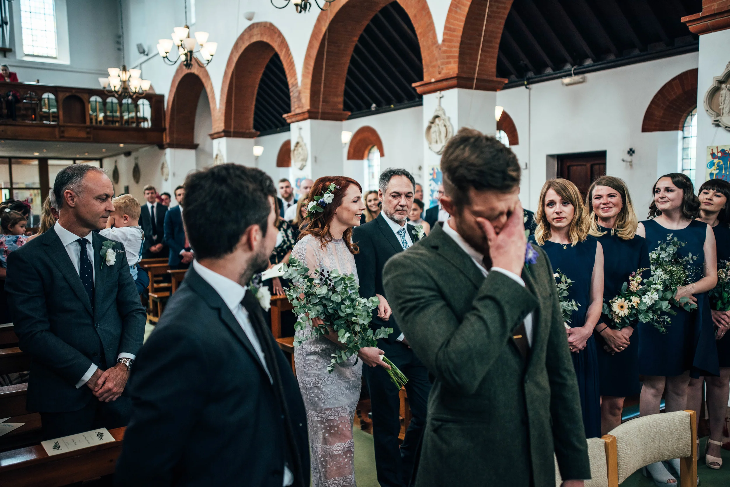 Essex UK Documentary Wedding Photographer Bride in non-white alternative Boho Vintage Dress walks down Aisle as Groom cries