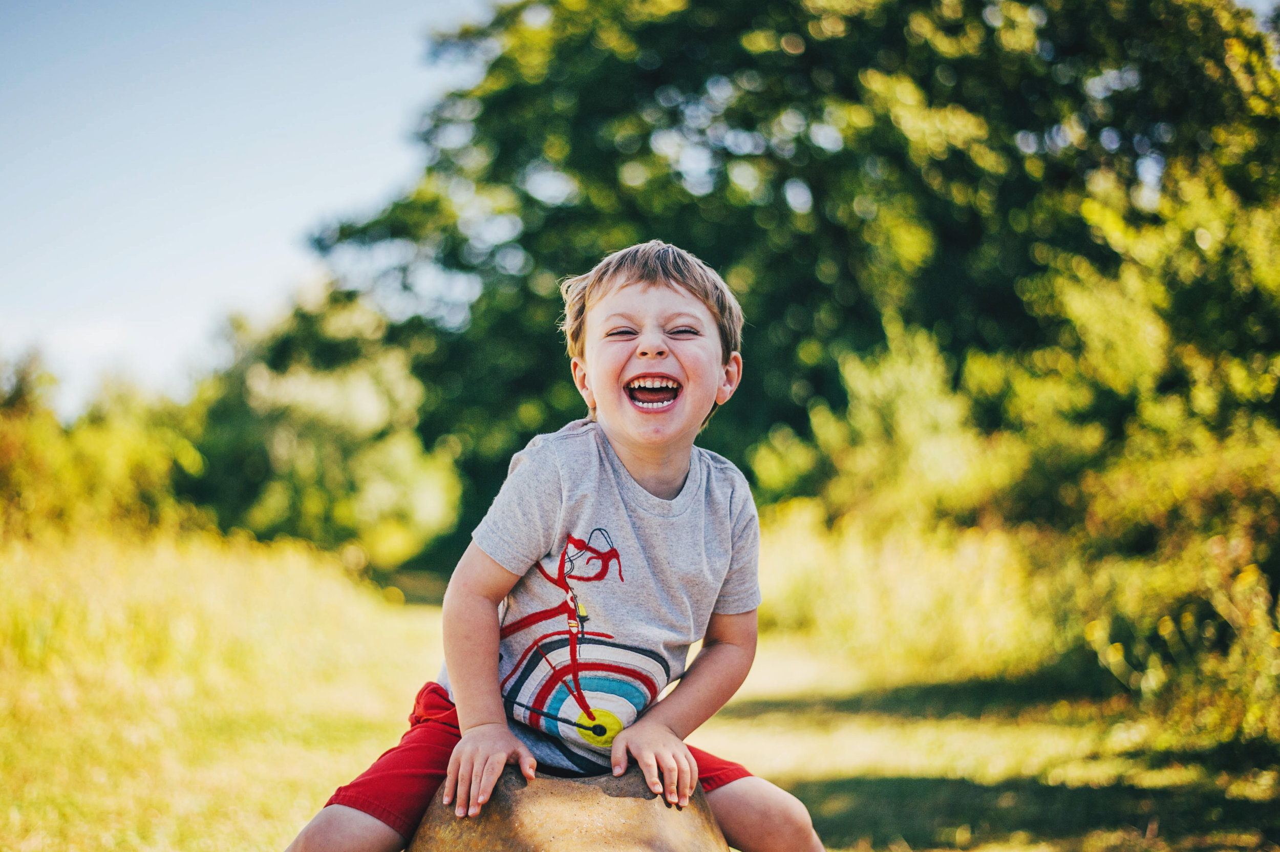 Little boy laughs in sunny park Essex UK Documentary Natural Portrait Photographer 