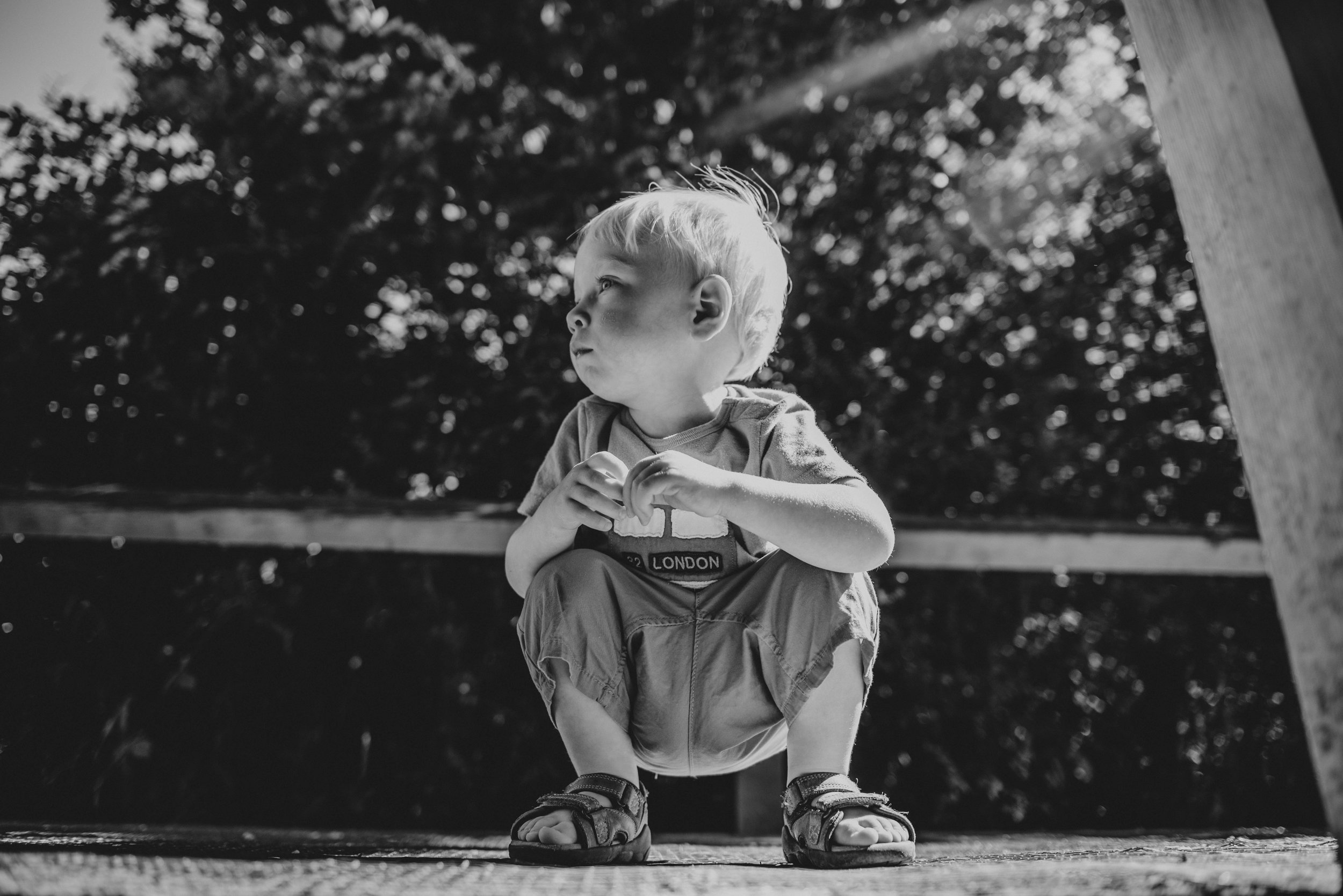 Little boy crouches on bridge sunny park Essex UK Natural Documentary Portrait Photographer