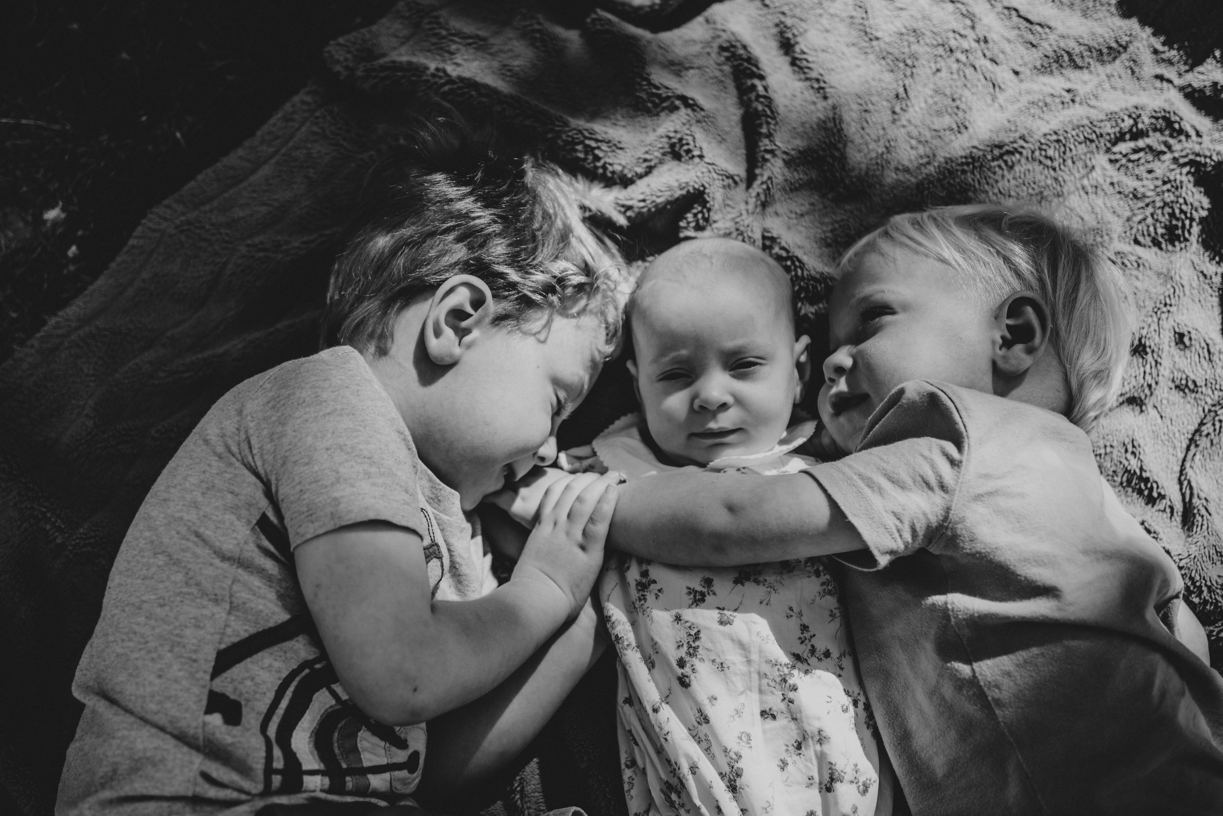 Big brothers hug baby sister Natural Documentary Portrait Photographer Essex UK