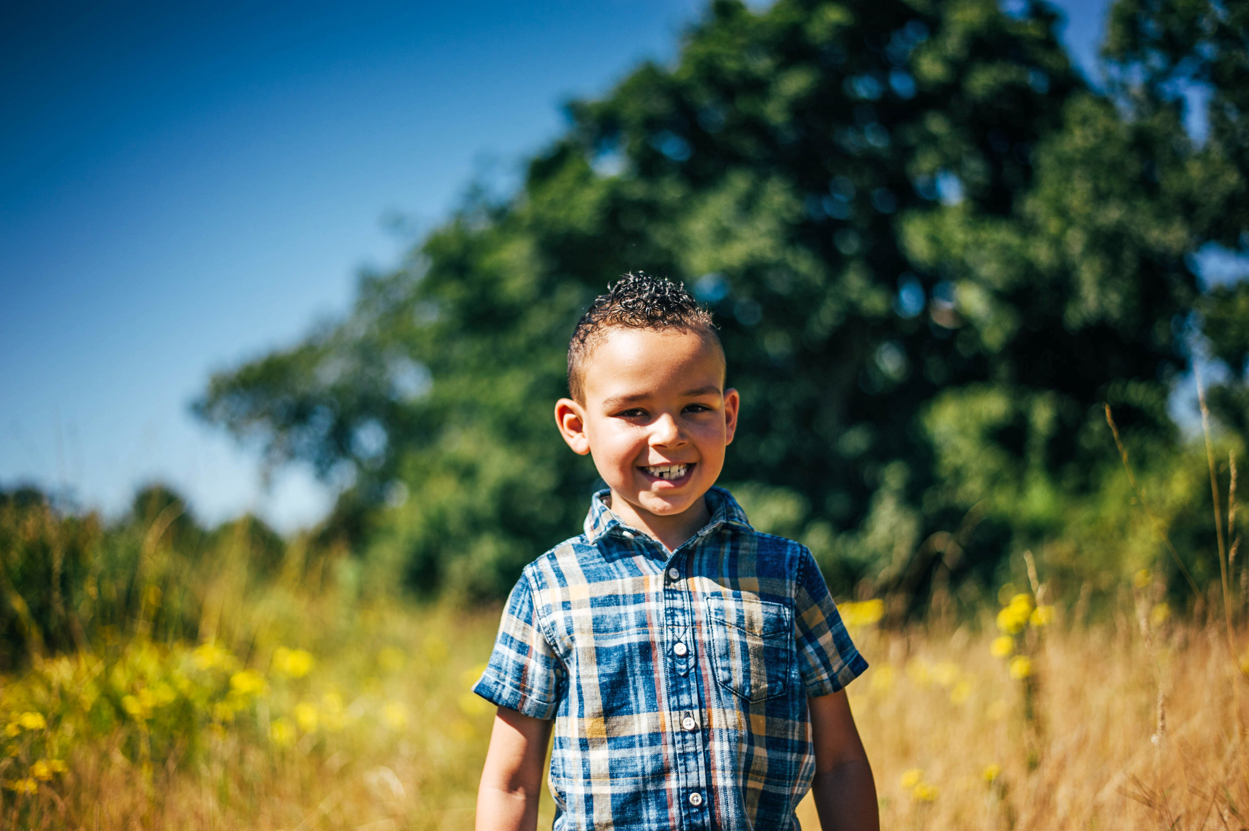 Boy smiles in long grass Essex UK Natural Documentary Portrait Photographer