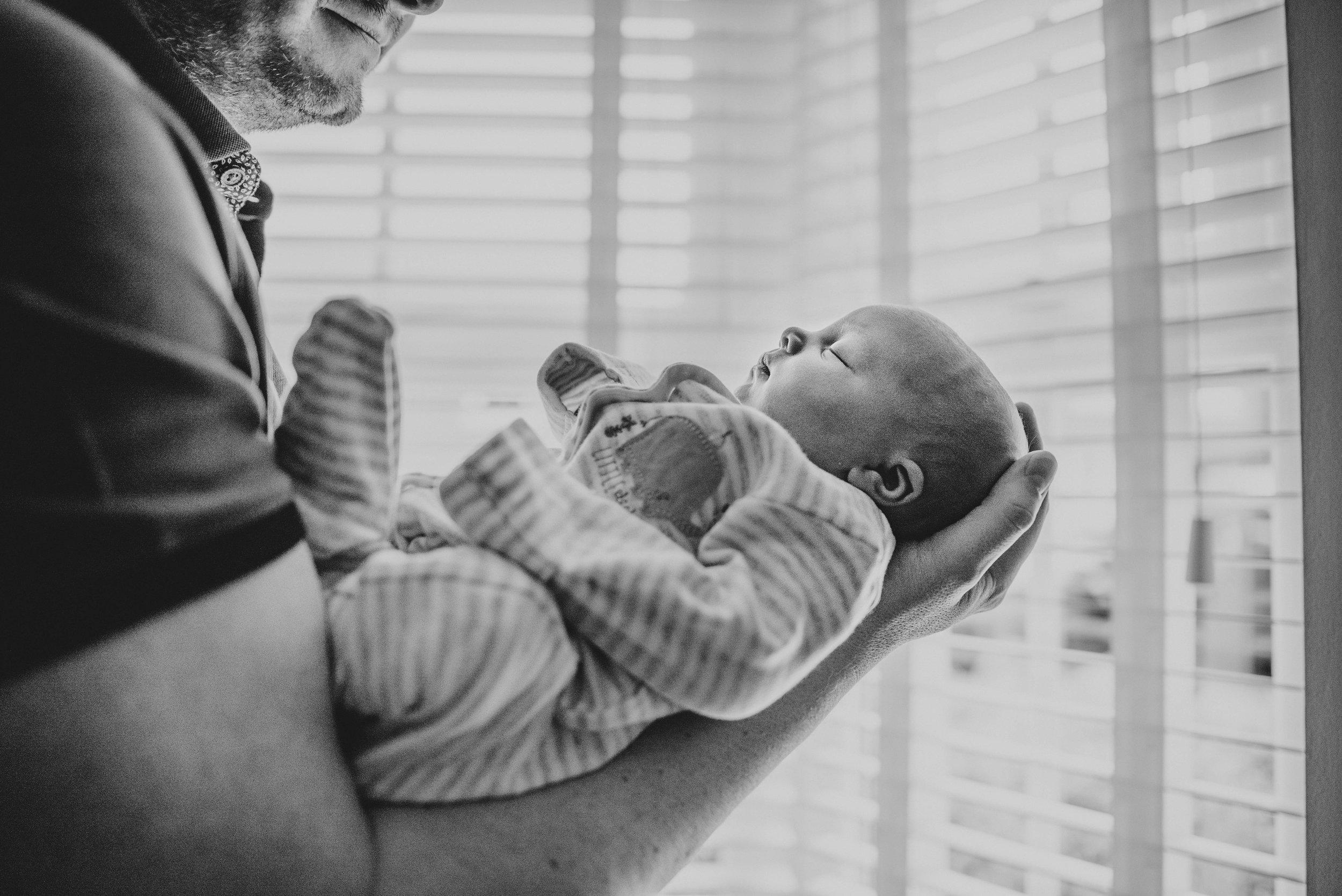 New Dad holds baby girl in windows light At Home Lifestyle Shoot Essex UK Documentary Portrait Photographer