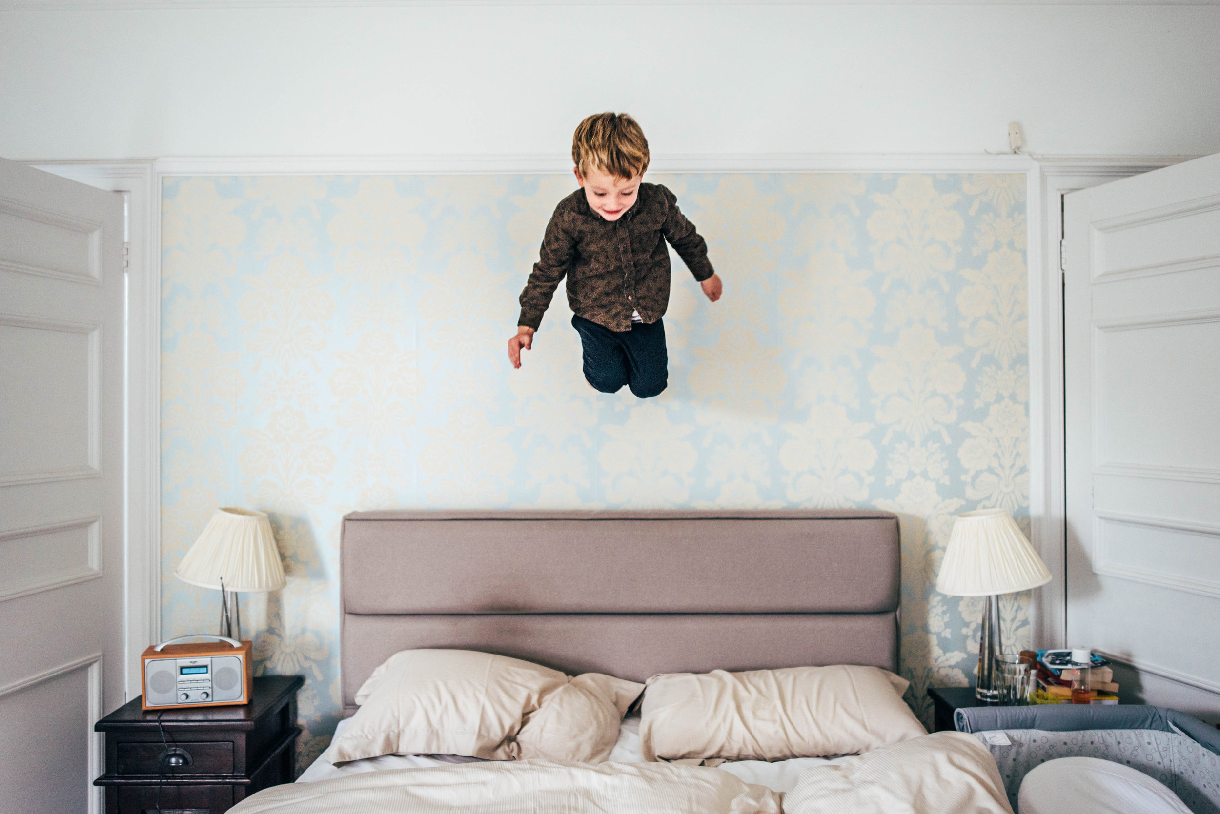 Little Boy mid air jumps on bed At Home Lifestyle Shoot Essex UK Documentary Portrait Photographer