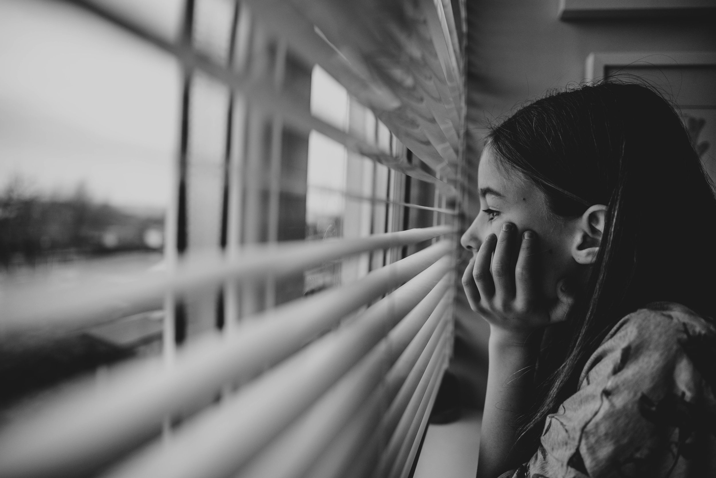 Girl looks out of window with blinds Essex UK Documentary Photographer