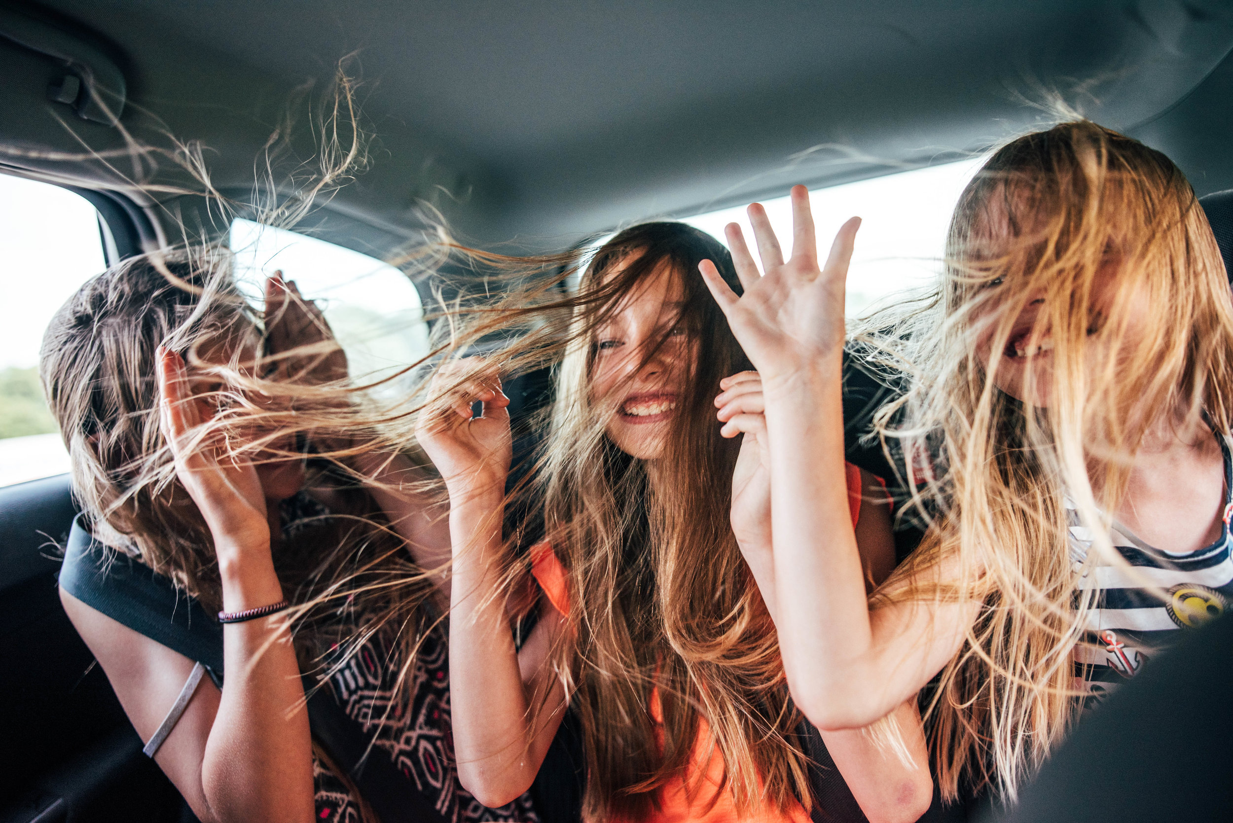 Three girls in back of a car with windows down, hair blowing Essex UK Documentary Portrait Photographer