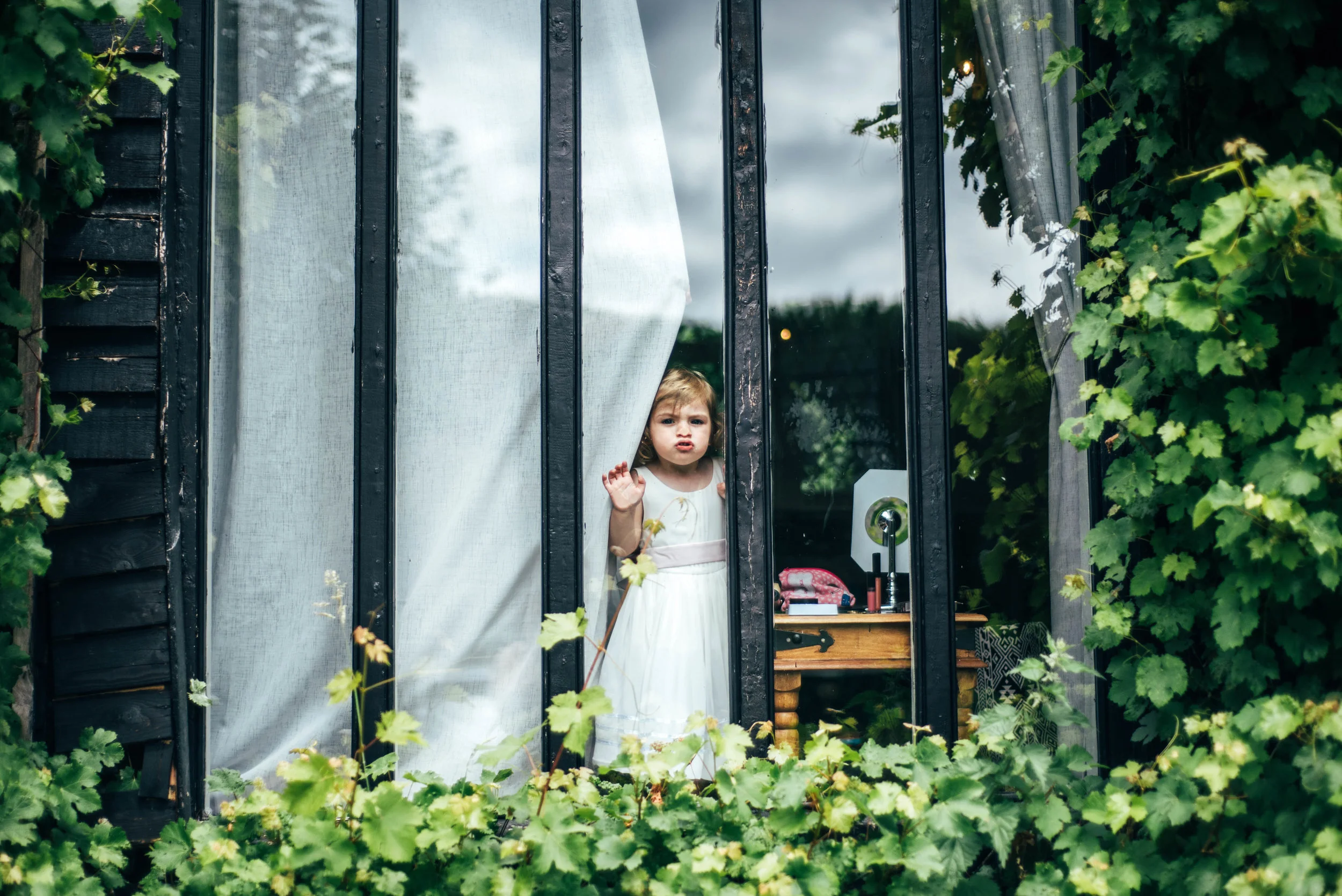 Flower girl squashes face against window Old Brook Barn Essex Documentary Wedding Photographer