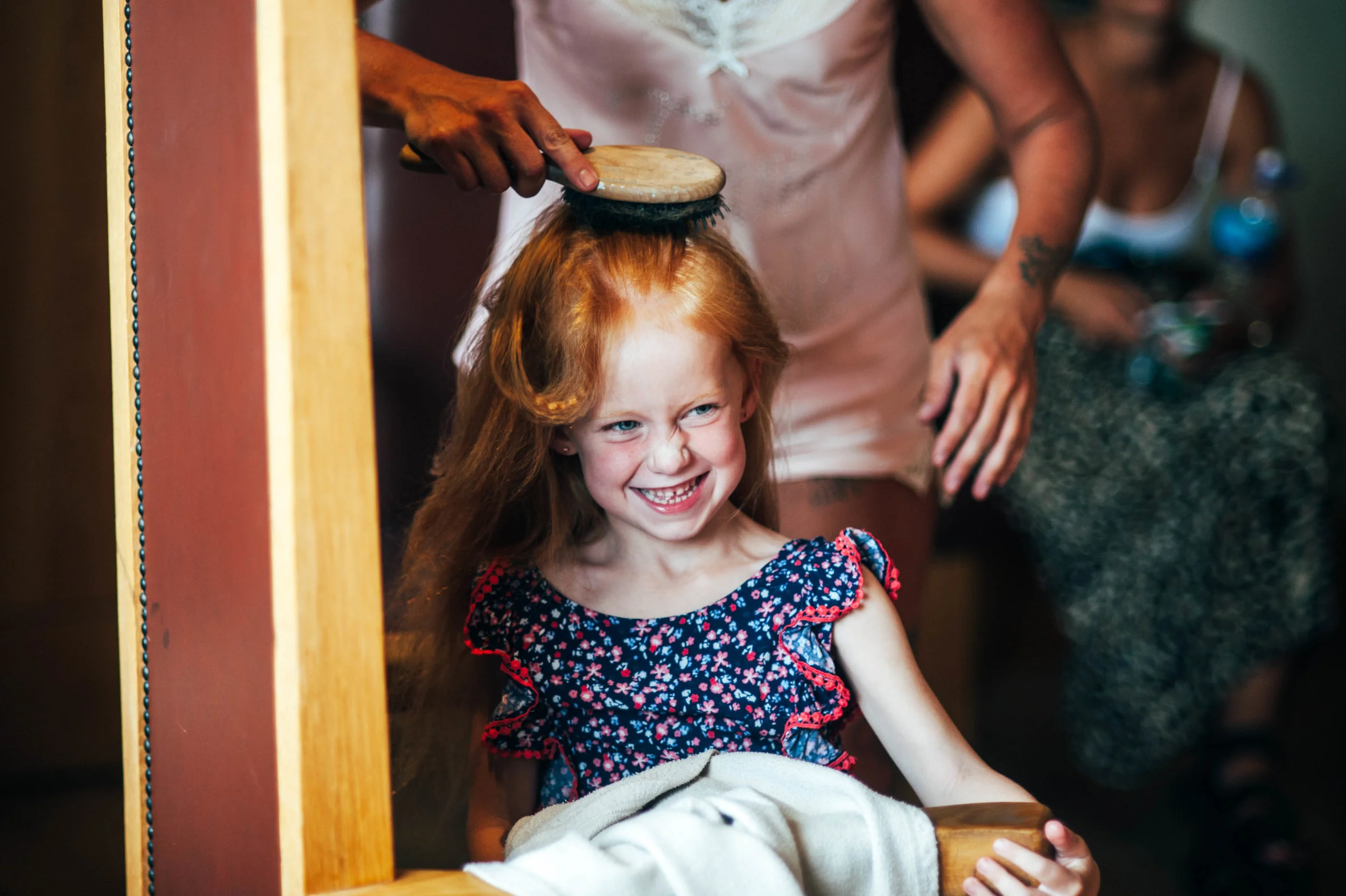 Flower girl smiles as her hair is brushed.  Stock Brook Manor, Billericay.  Essex Documentary Wedding Photographer