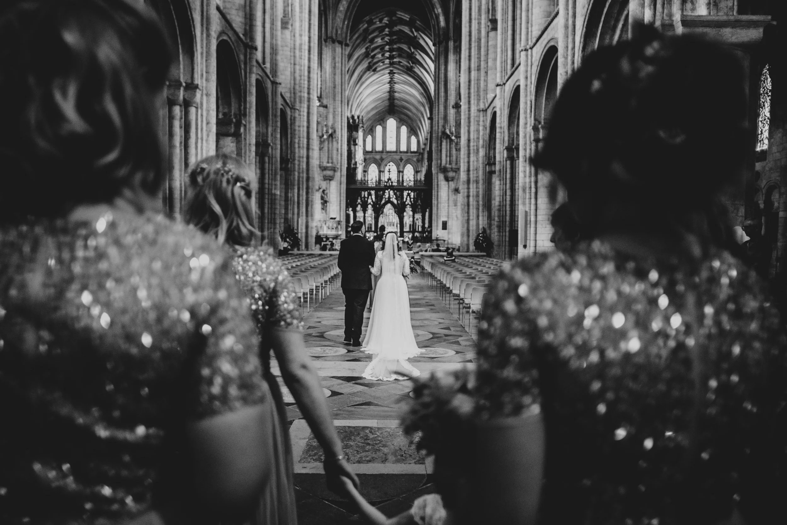 View between Bridesmaids of Bride walking down aisle in Ely Cathedral Cambridge, Essex Documentary Wedding Photographer