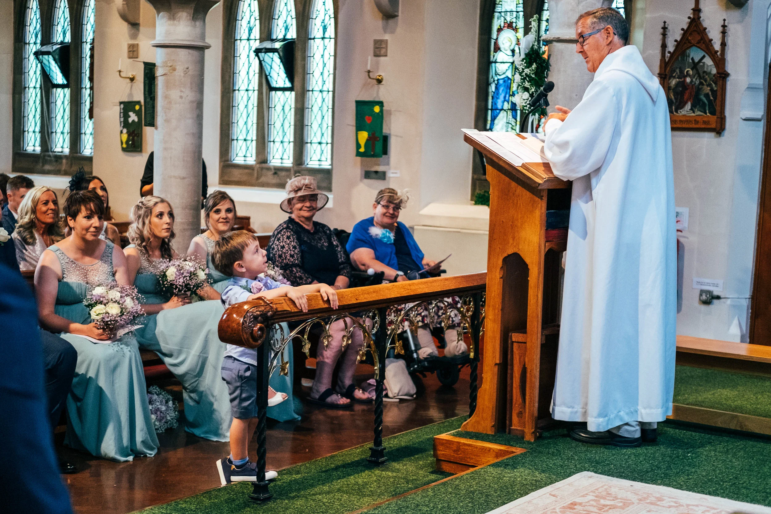 Little boys looks up at vicar during church wedding, Essex Documentary Wedding Photographer
