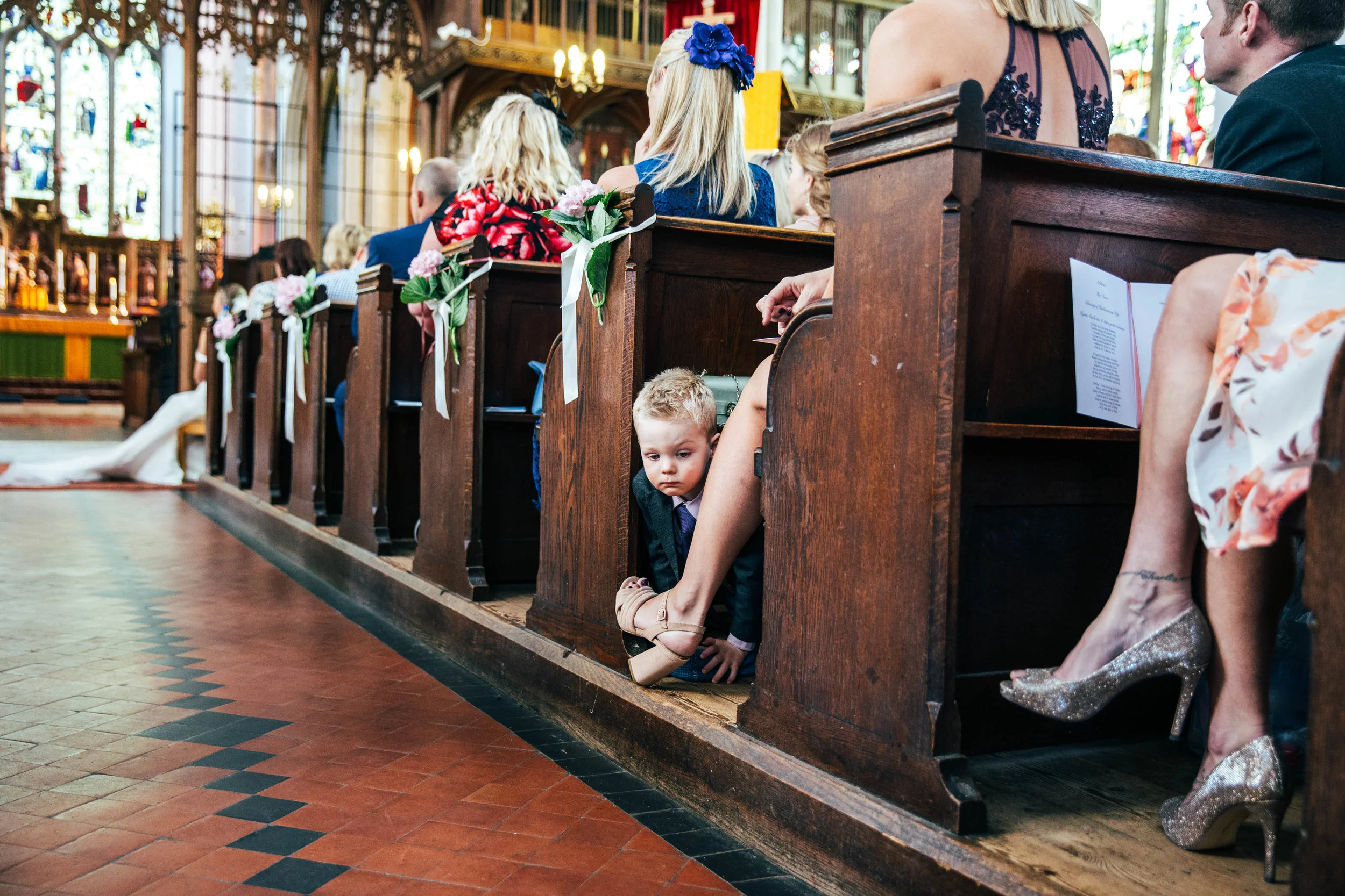 Little boy peeks out of pew in St Mary's Church, Bocking for Fennes, Braintree Wedding Essex Documentary Wedding Photographer 