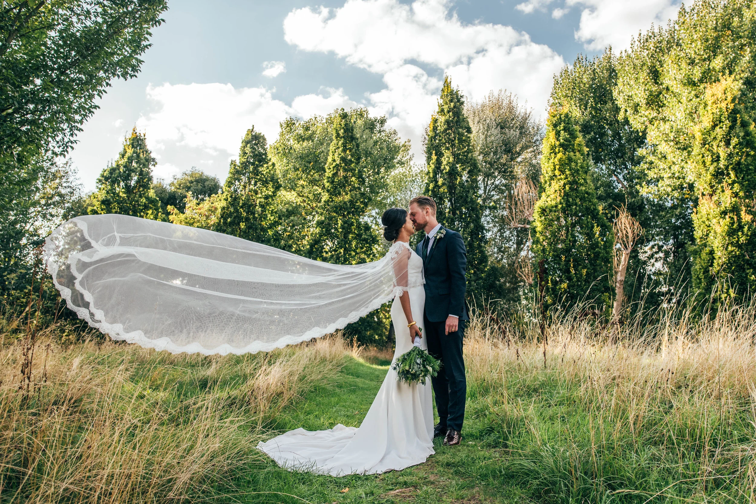 Bride with windswept veil kisses Groom at Mile End Ecology Pavilion.  Essex Documentary Wedding Photographer