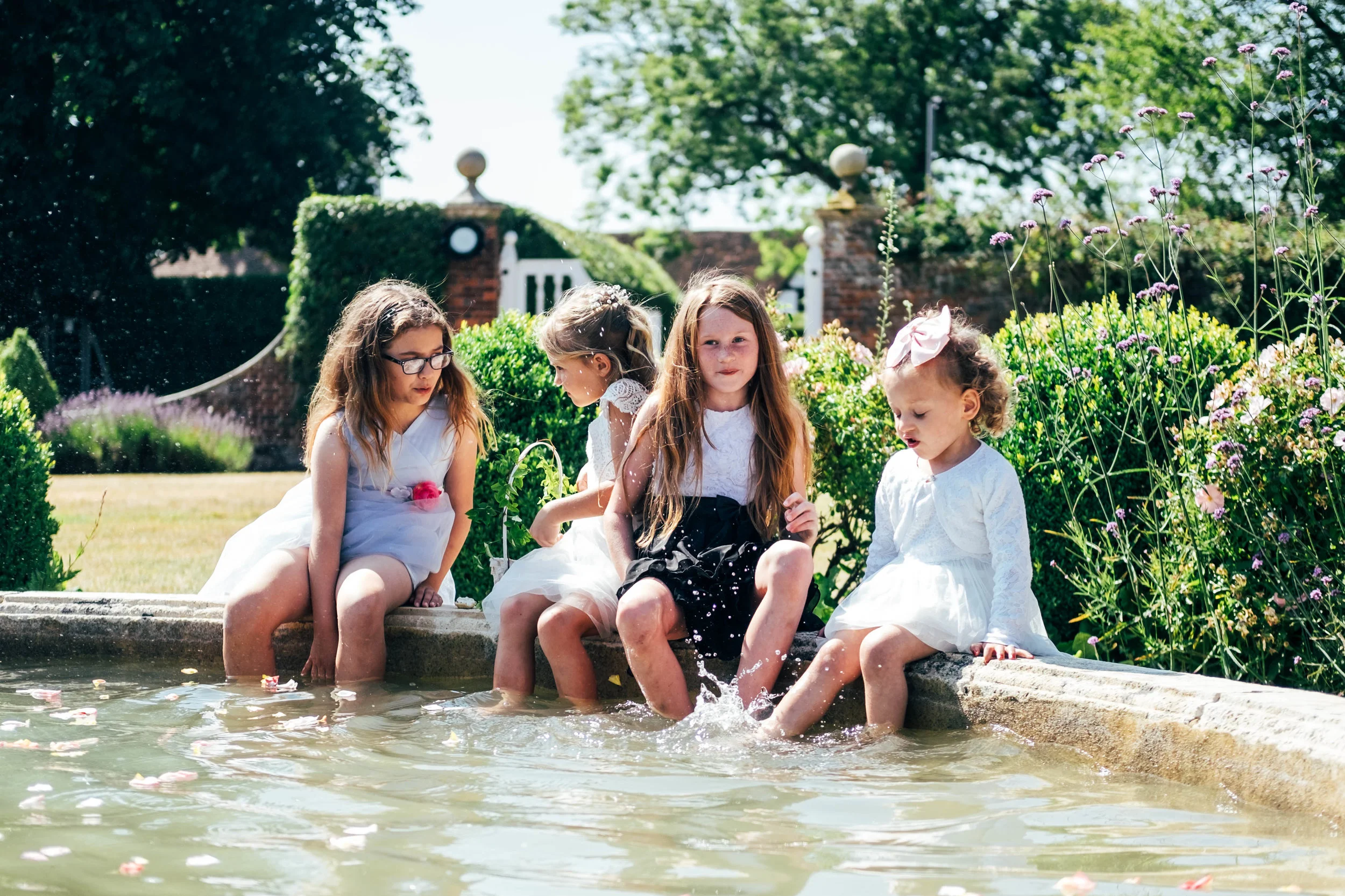 Little girls sit in Fountain for hot summer wedding at Quendon Hall.  Essex Documentary Wedding Photographer