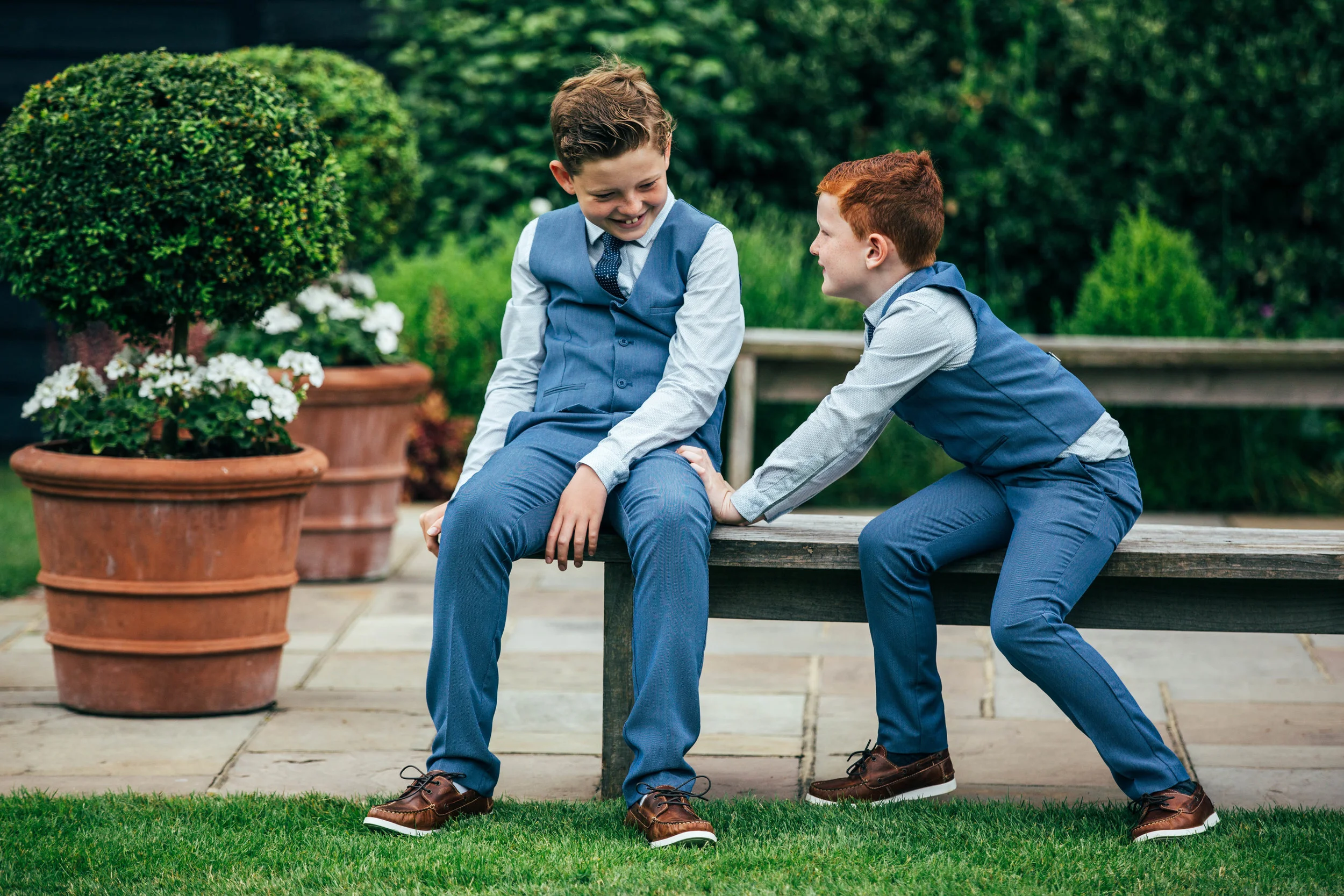 Boy tries to push his brother off bench at Blake Hall, Ongar.  Essex Documentary Wedding Photographer