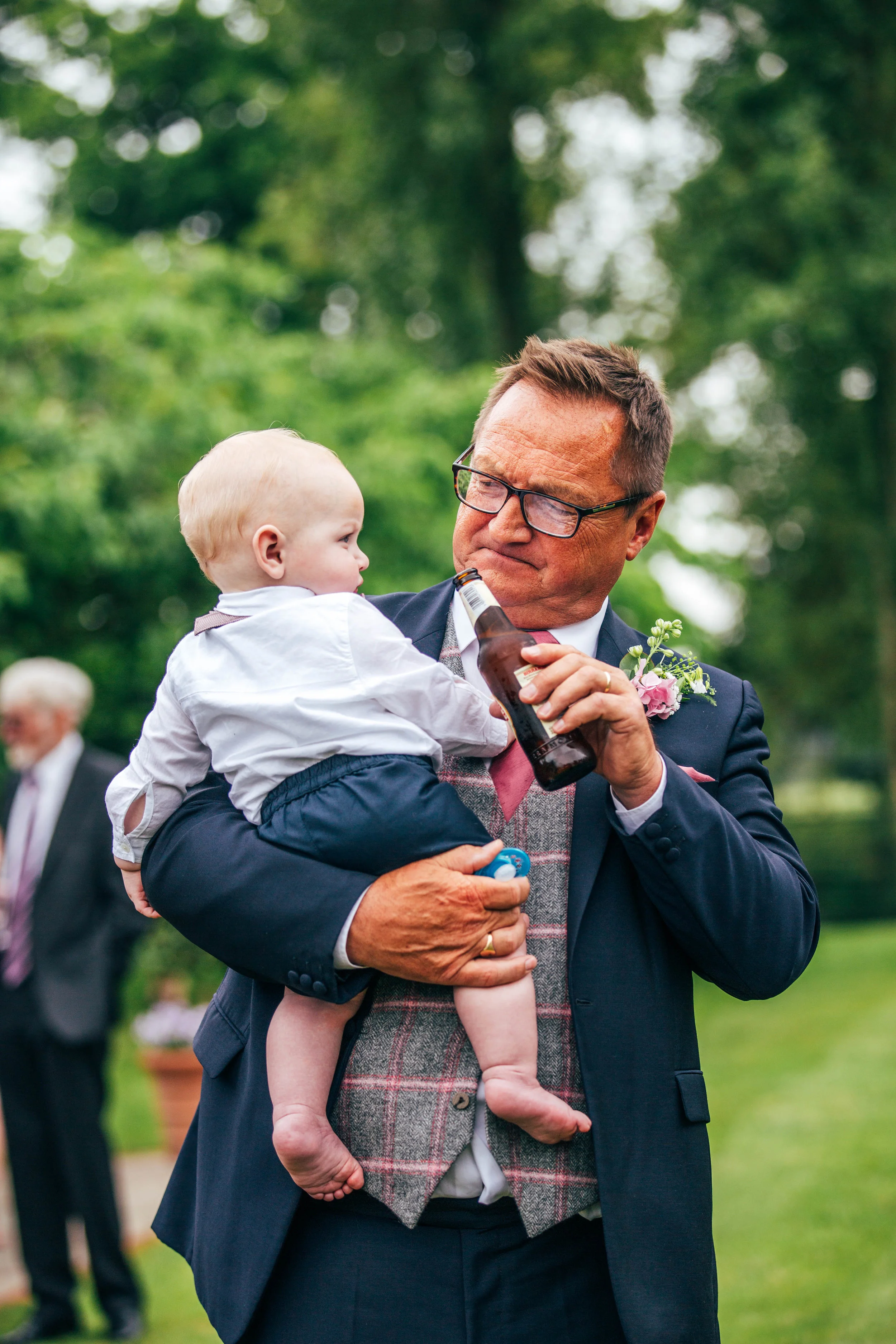 Wedding guest shows baby a beer at Blake Hall, Ongar.  Essex Documentary Wedding Photographer