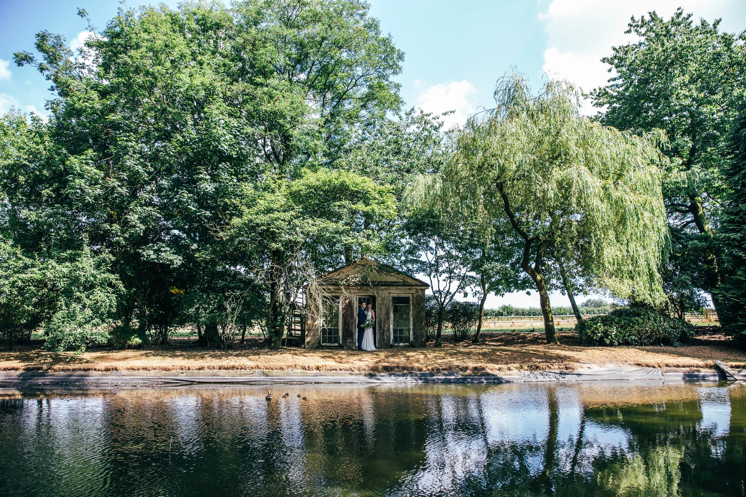 Bride and Groom by ruins over a lake, The long Barn.  Essex Documentary Wedding Photographer