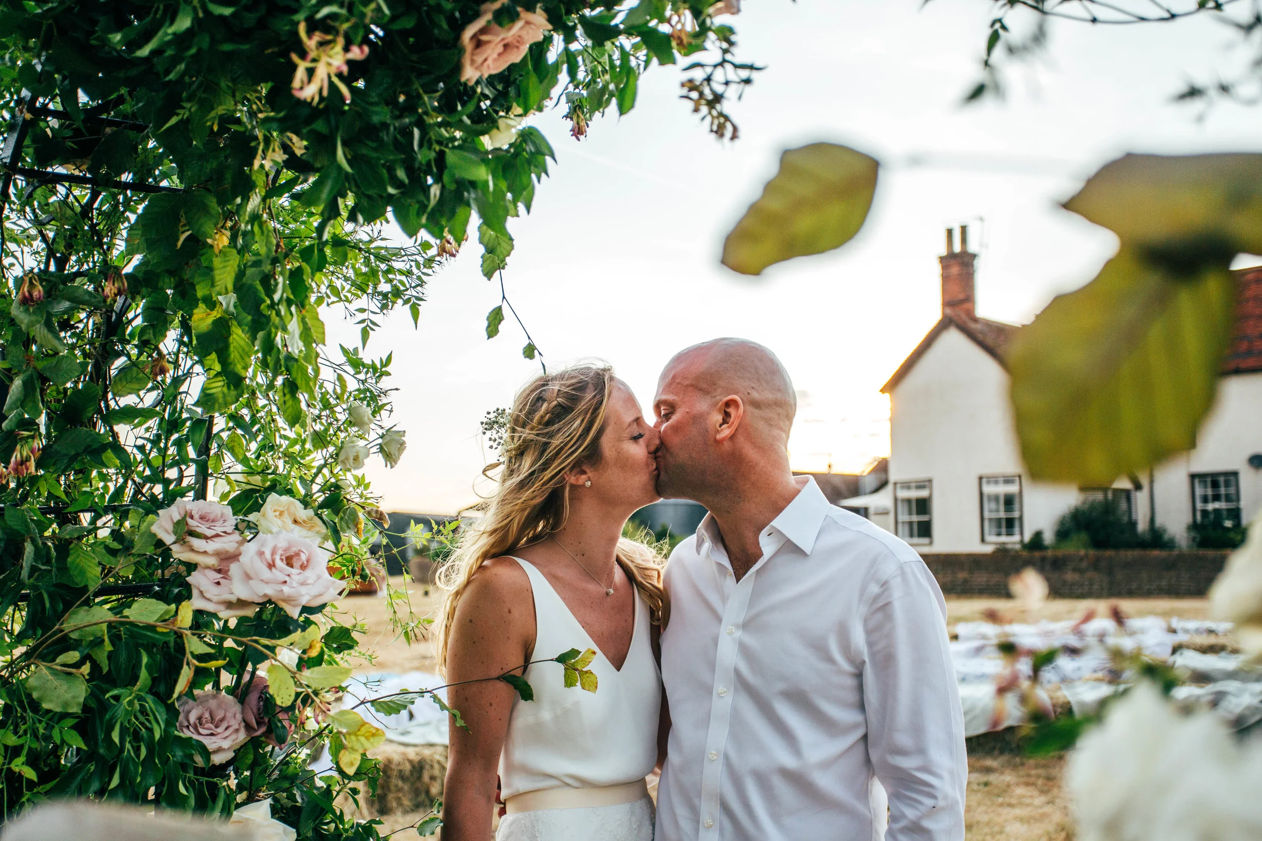 Bride and Groom kiss at Sunset under Flower Arch for outdoor, DIY Boho Wedding Essex Documentary Wedding Photographer