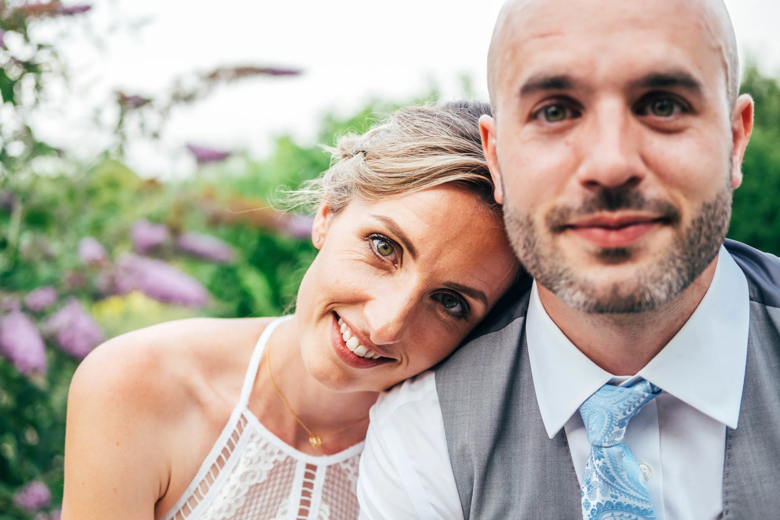 Bride looks at camera leaning on Grooms shoulder, DIY Outdoor wedding. Essex Documentary Wedding Photographer