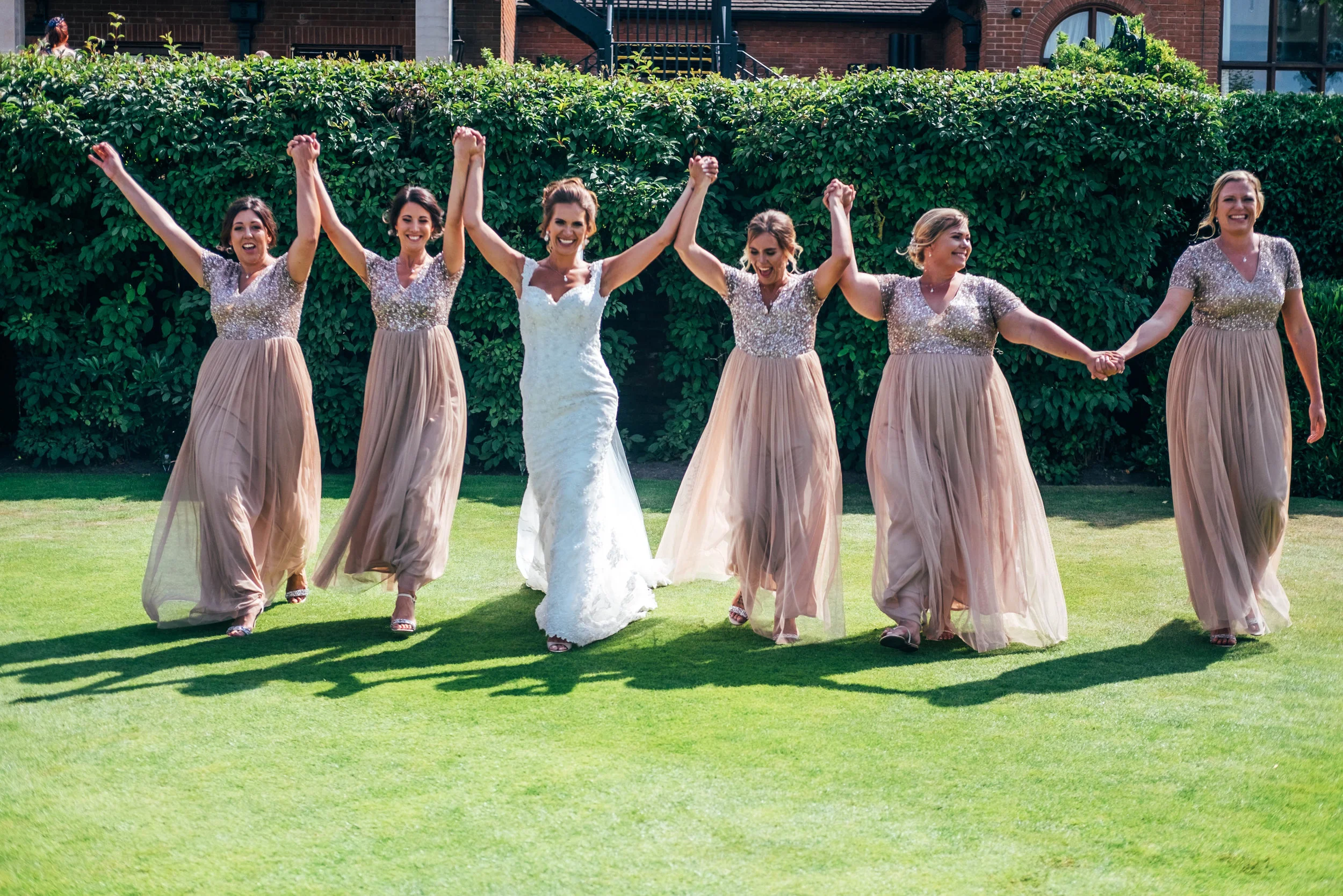 Bride and Bridesmaids cheer and raise arms on lawn at Stock Brook Manor, Billericay, Essex Documentary Wedding Photographer