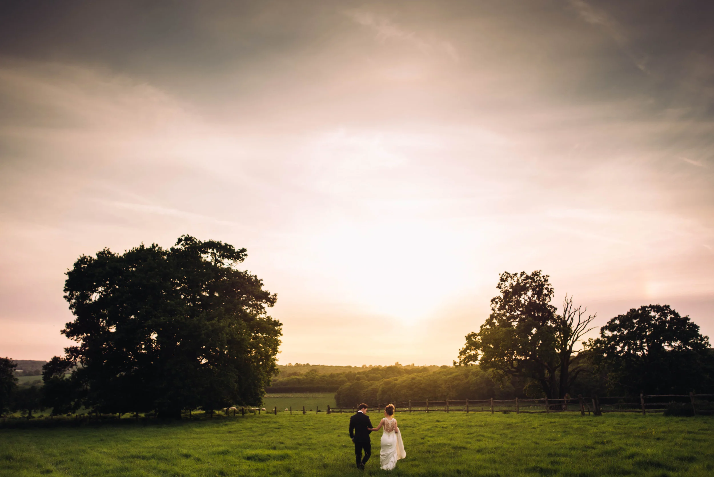 Bride and Groom walk in field at sunset at Gaynes Park, Epping, Essex Documentary Wedding Photographer