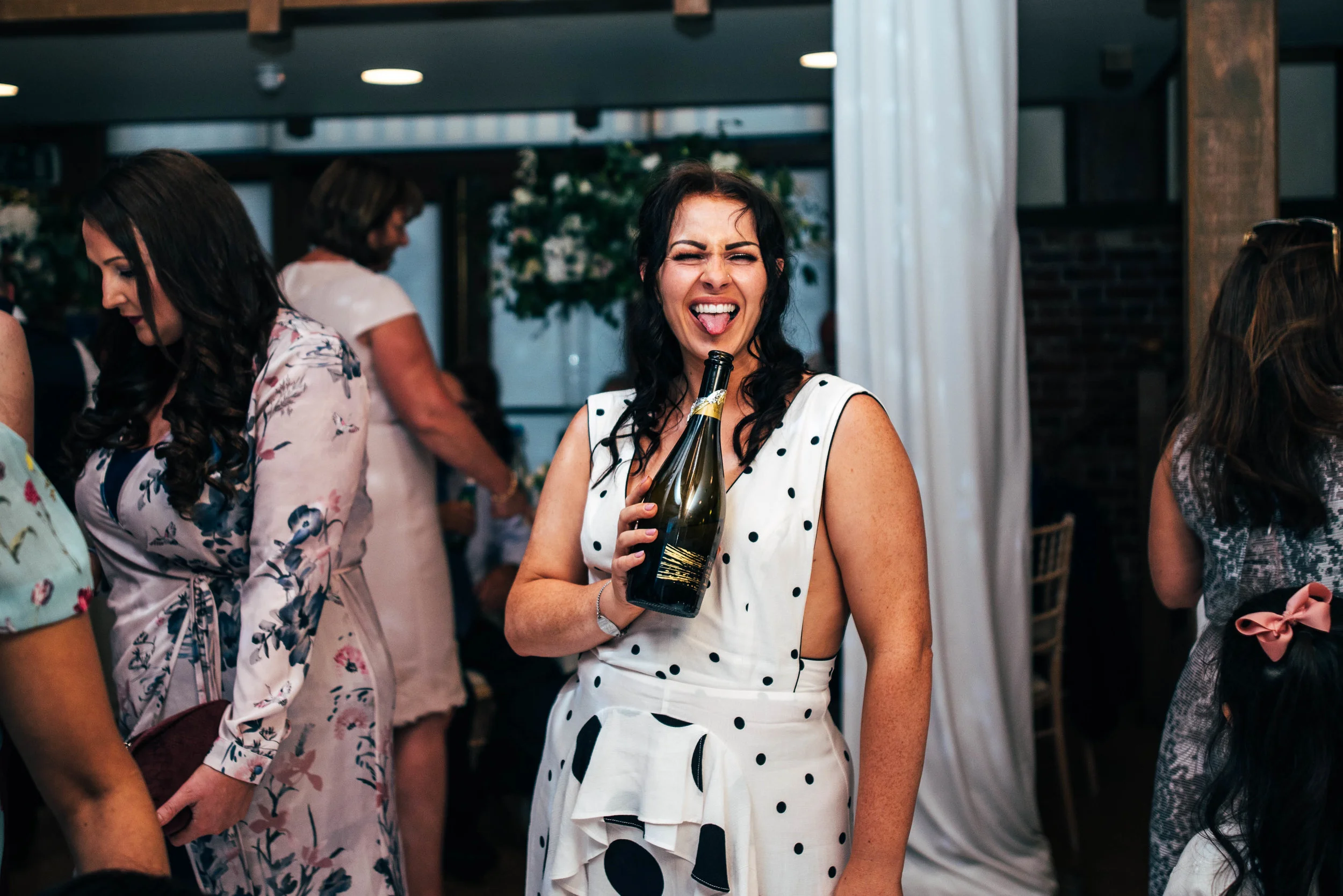 Tipsy wedding guests pokes out tongue and holds champagne bottle at Gaynes Park, Epping.  Essex Documentary Wedding Photographer