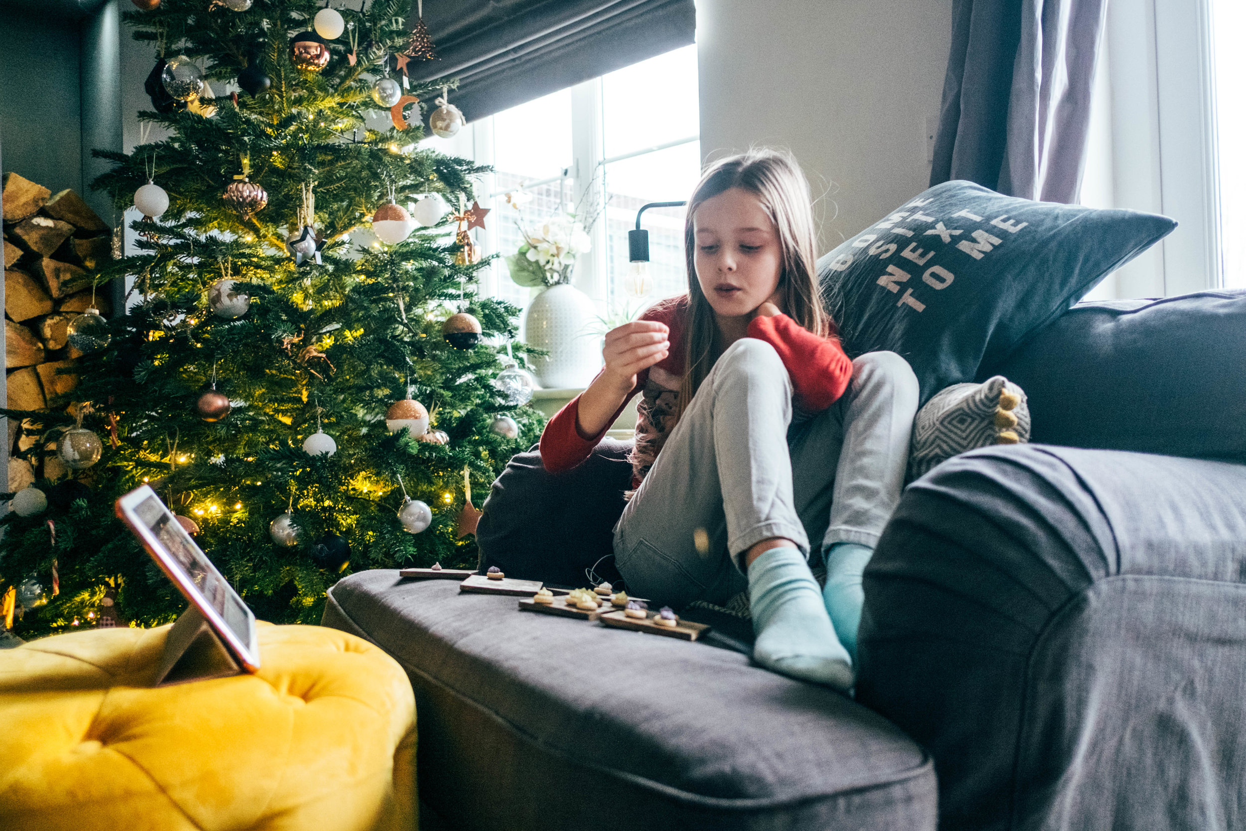 Little girl sits on chair by Christmas tree, Essex Documentary Wedding Family Photographer