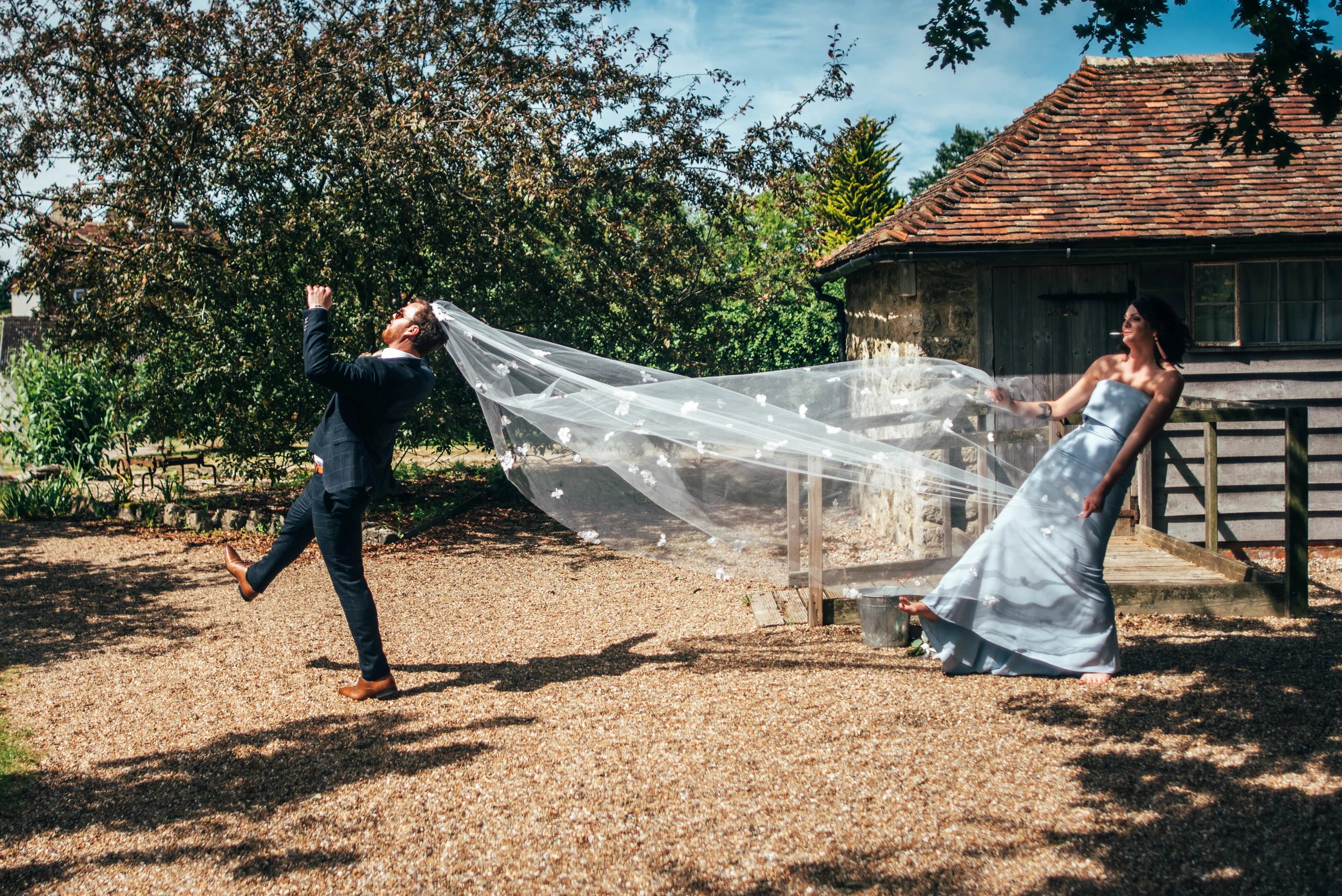 Smoking Bridesmaid pulls on veil worn by Groom at Ratsbury Barn Essex Documentary Wedding Photographer