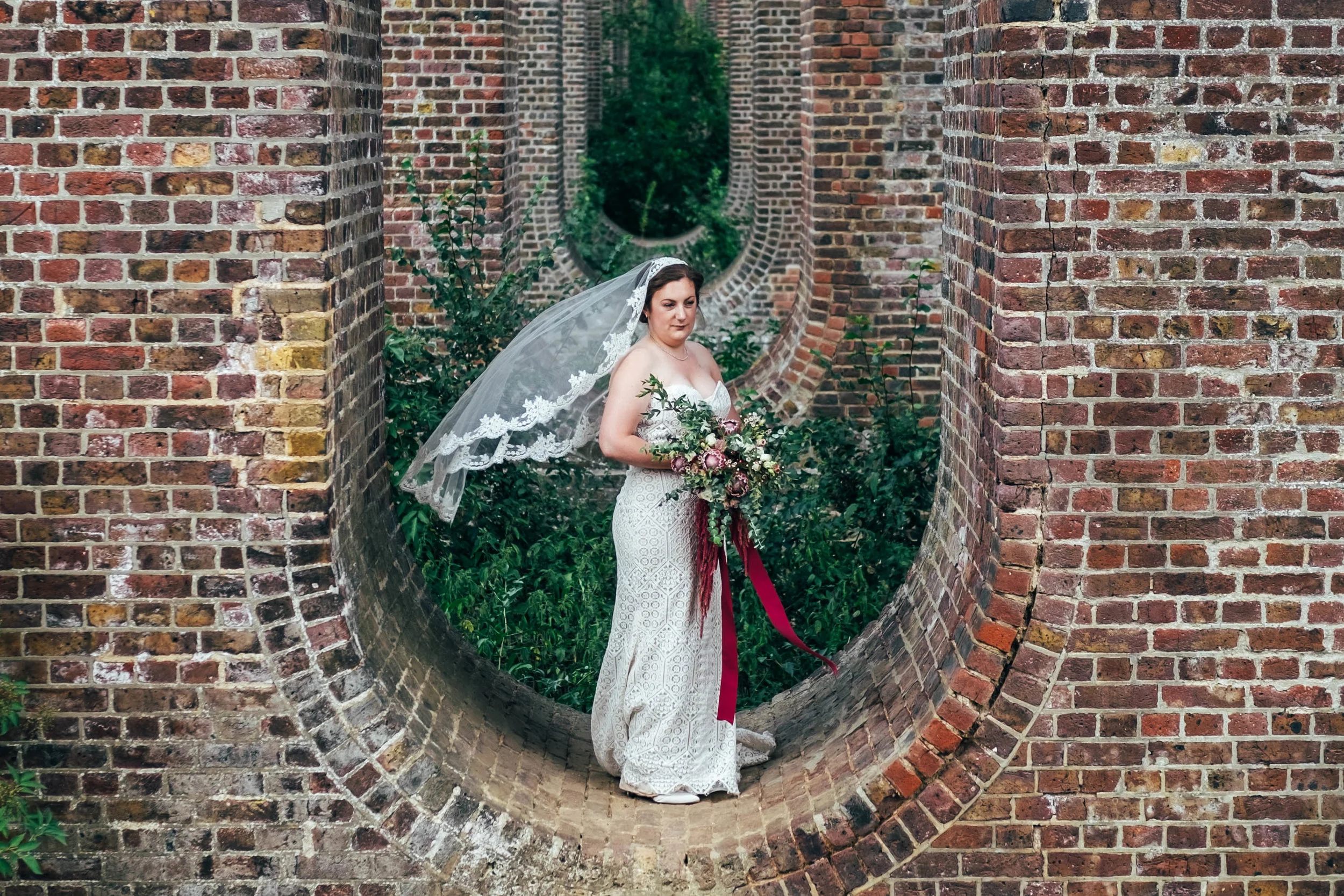 Bride in long veil stands in viaduct East Anglian Railway Museum Essex Documentary Wedding Photographer