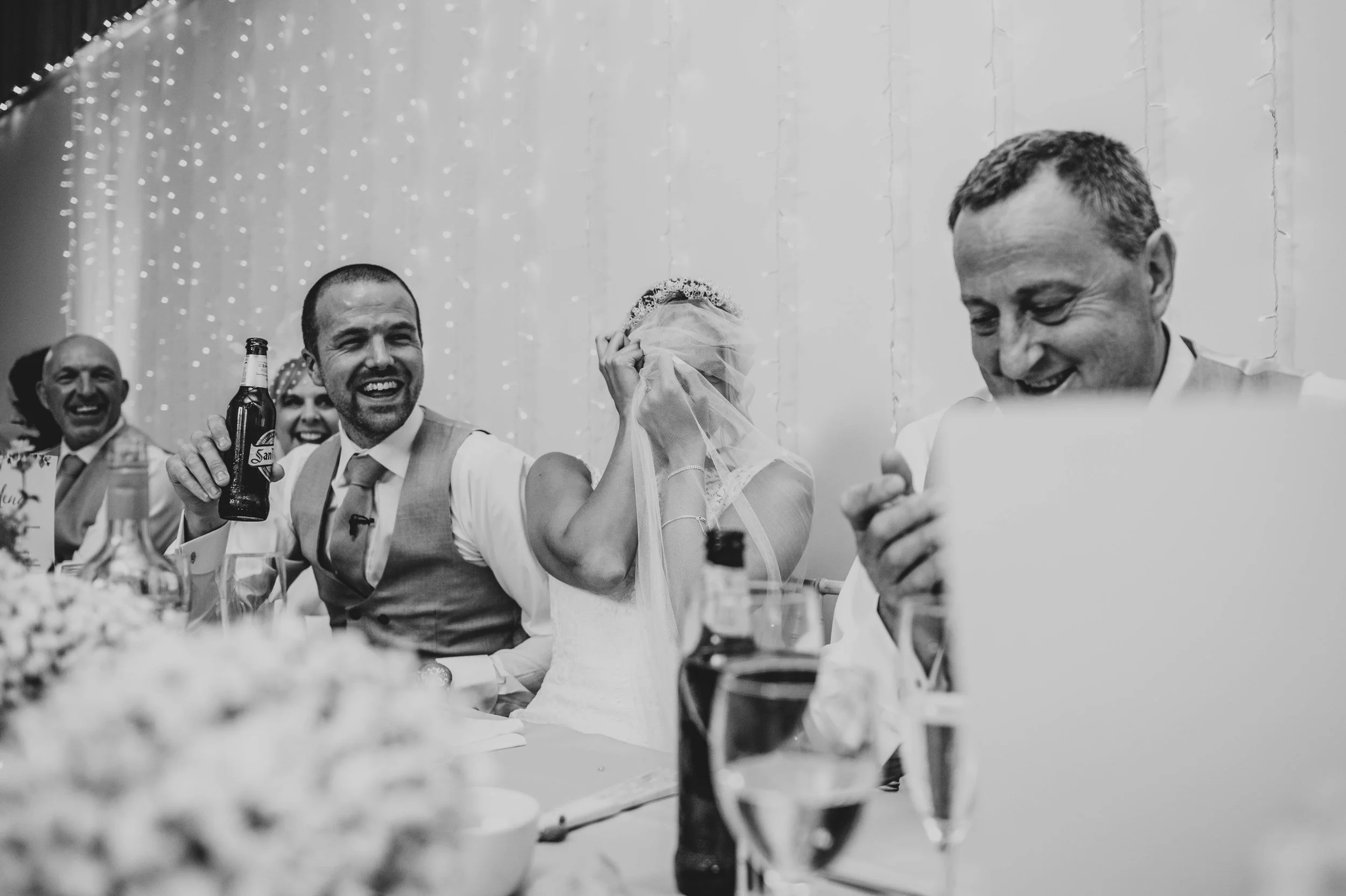 Embarrassed Bride hides her face in her veil during speeches at Houchins Coggeshall Essex Documentary Wedding Photographer