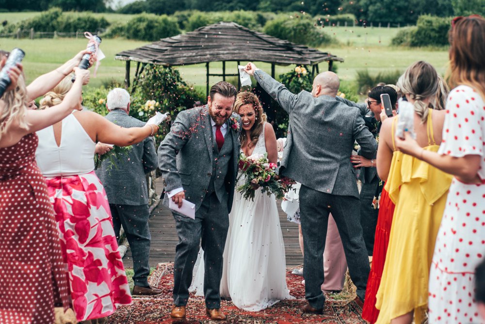 Lush, Vibrant Reds and Tweed for a Movie inspired Barn wedding at The House Meadow with Bridesmaids in Jumpsuits and a Festival Vibe. Essex Documentary Wedding Photographer