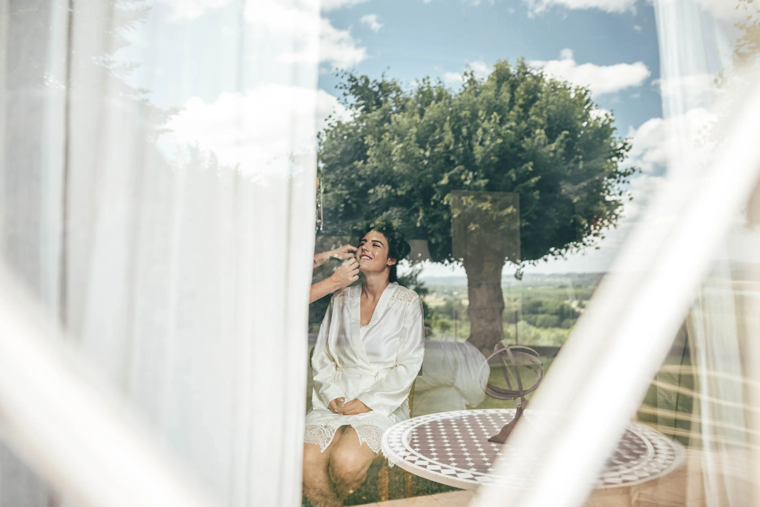 Bride preps at a window with a reflection at Chateau Soulac, Dordogne. Essex Documentary Wedding Photographer. Three Flowers Photography